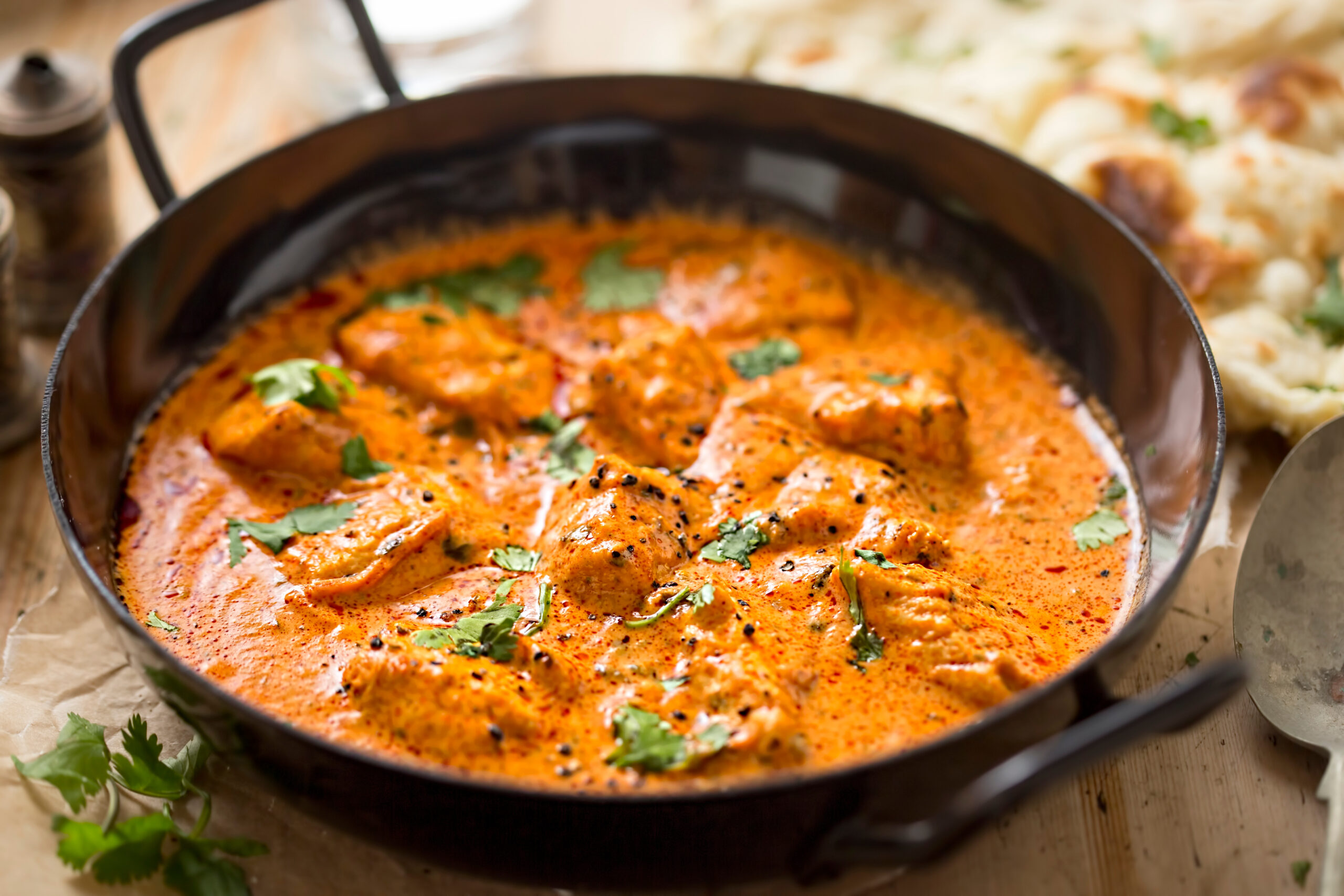 Butter chicken in a black pan with naan bread
