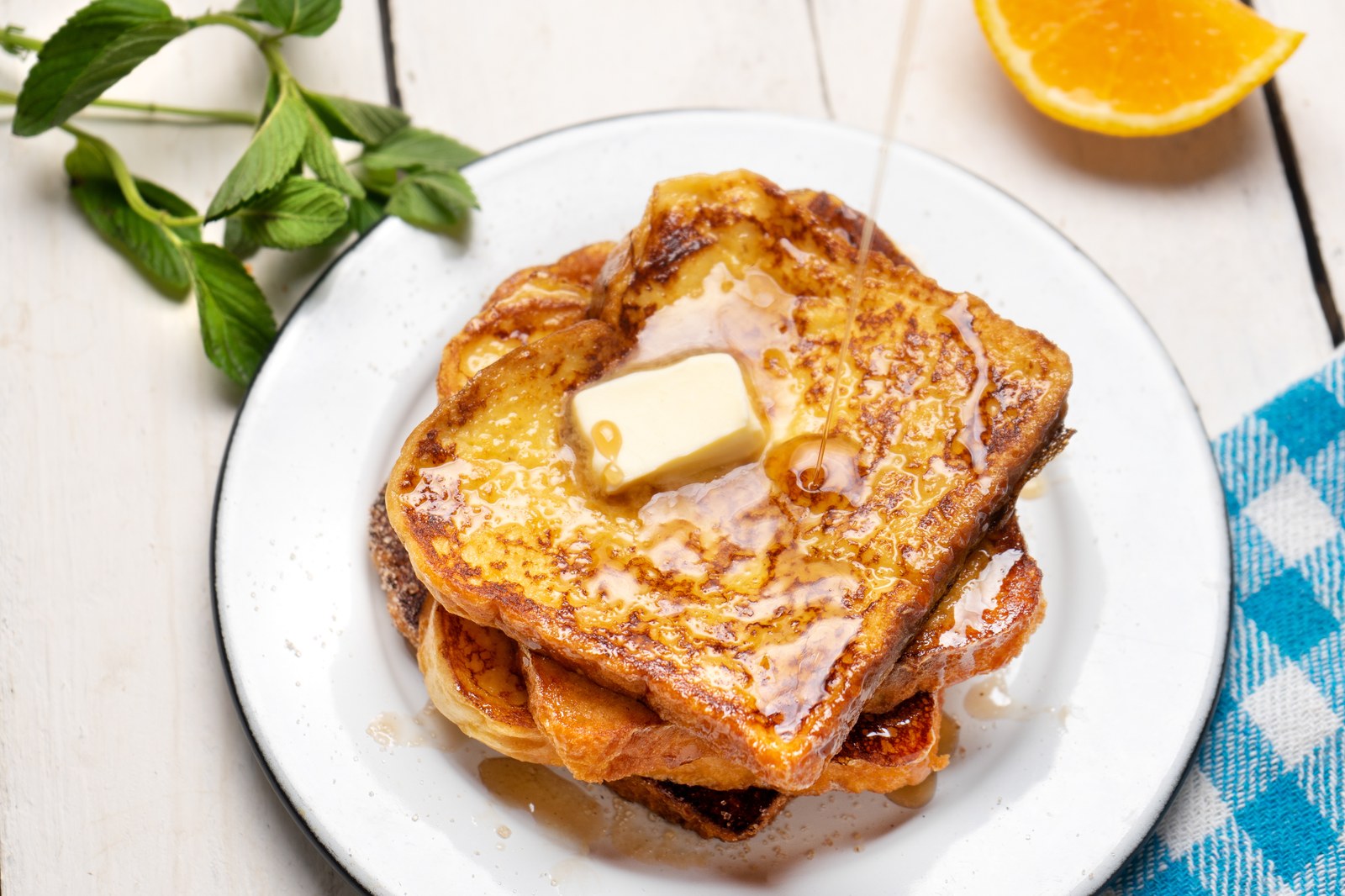 Stack of golden brown French toast with butter pat and maple syrup drizzled on top