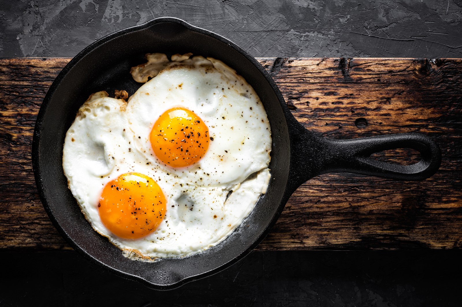 Golden fried eggs with crispy lace edges and runny yolks in a nonstick skillet with melted butter