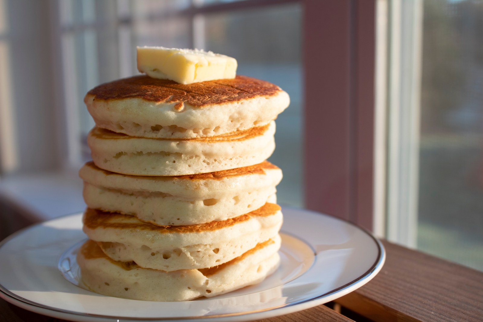 Stack of five fluffy buttermilk pancakes with pat of butter on top on white plate