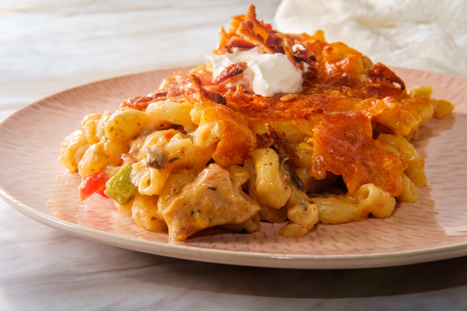 Butter chicken mac and cheese with creamy curry sauce, elbow pasta, tender chicken pieces, bell peppers, topped with golden crispy onions and white sour cream dollop on pink ceramic plate