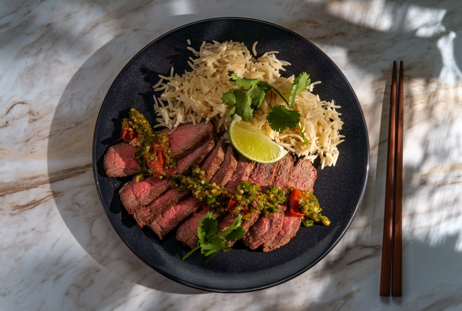 Thai crying tiger beef sliced and plated with rice and green chili dipping sauce, garnished with cilantro and lime