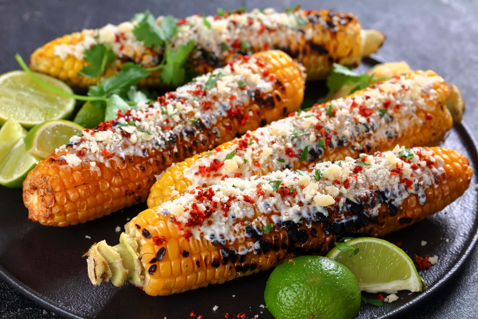 Grilled Mexican street corn coated with crema, cotija cheese, chili powder, and cilantro with lime wedges
