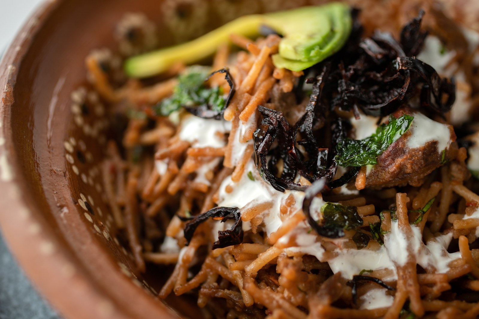 Bowl of fideo seco with toasted pasta noodles, dried chilies, crema drizzle, and avocado slices