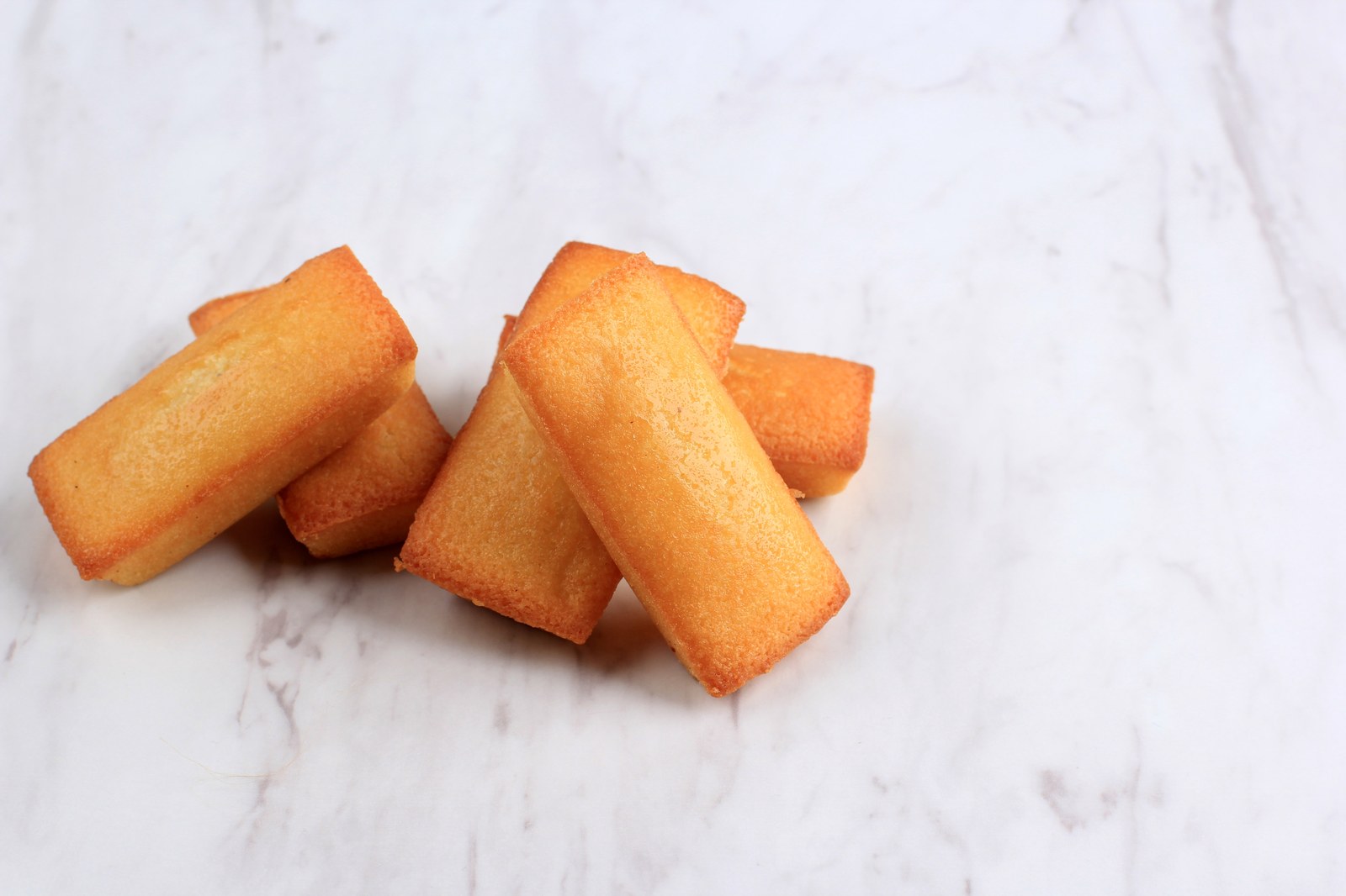 Four golden brown French financier cakes with their characteristic rectangular shape on white marble