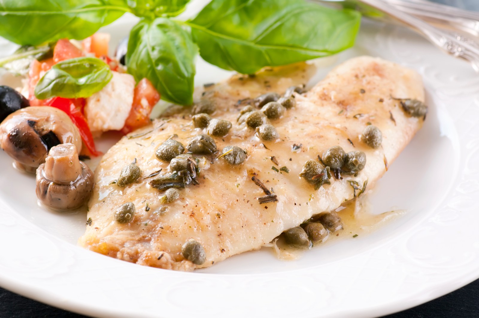White fish fillet in lemon butter sauce with capers, served with a side salad of shrimp, tomatoes, and basil