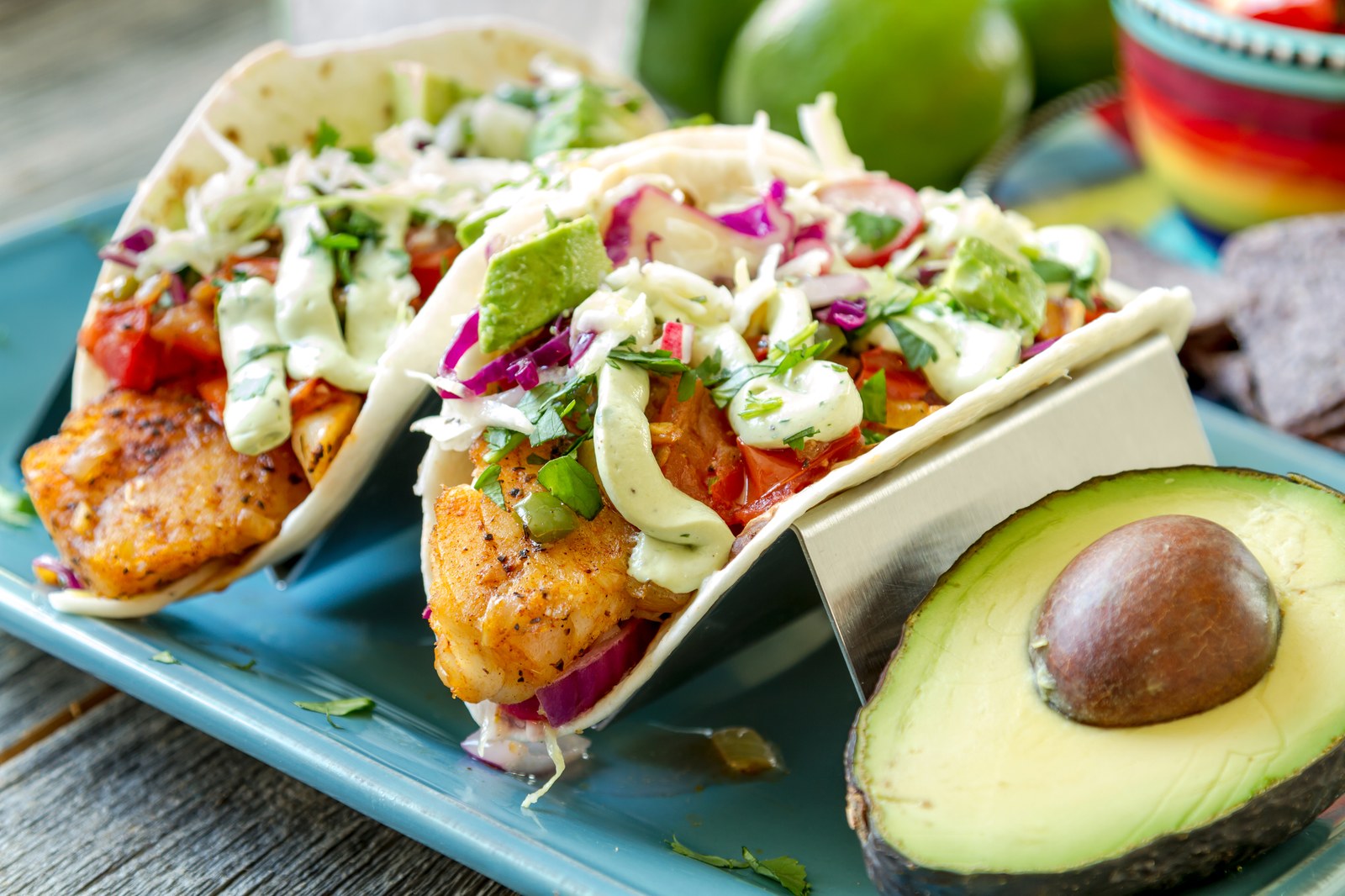 Two crispy fish tacos topped with cabbage slaw, crema, cilantro, and diced tomatoes, served with avocado halves