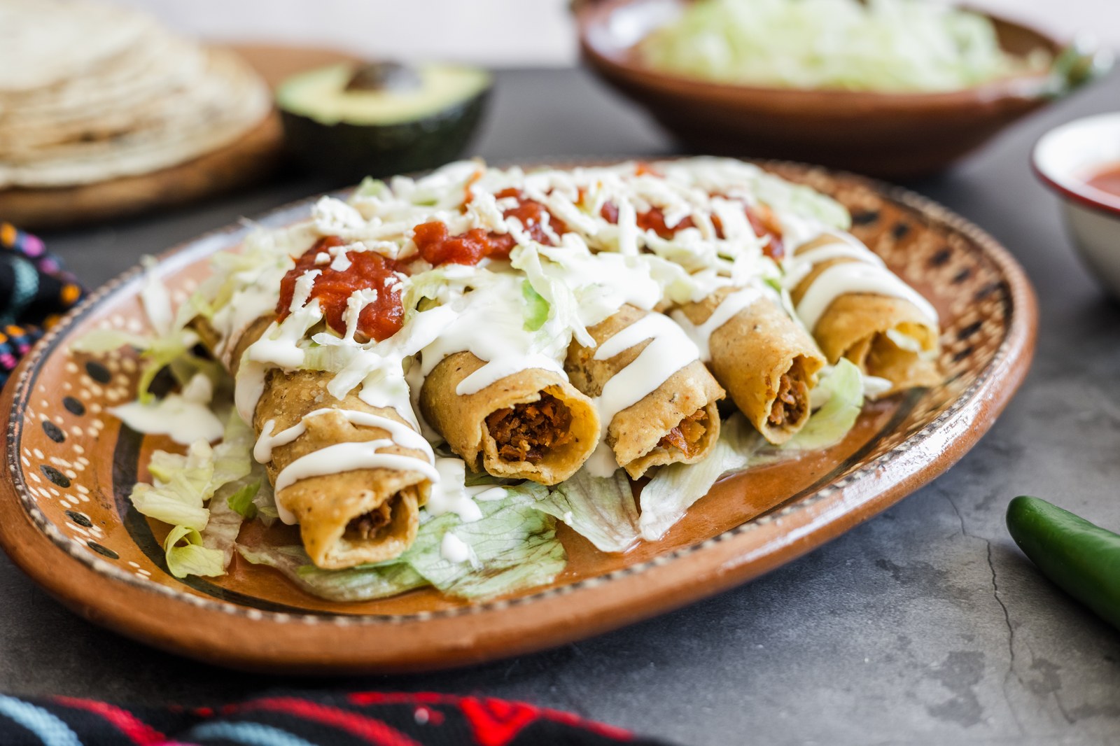 Mexican flautas, rolled and fried tortillas filled with meat, topped with crema, salsa, and shredded lettuce