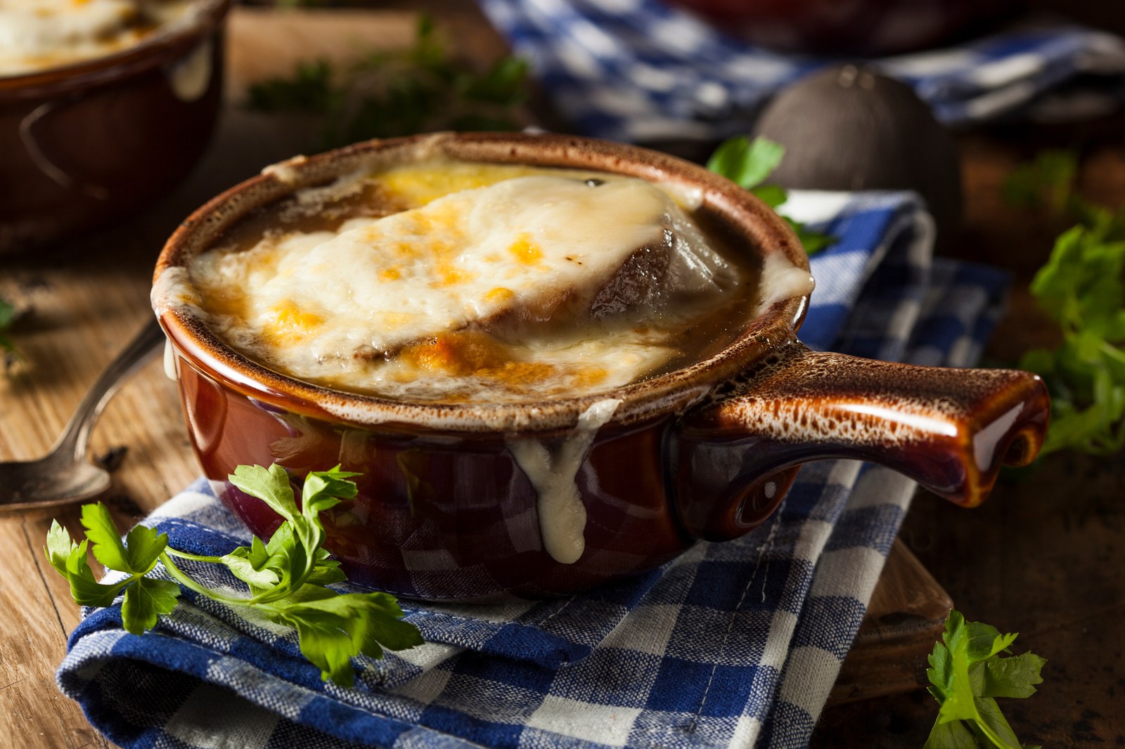 French onion soup in a brown ceramic crock with melted cheese on top