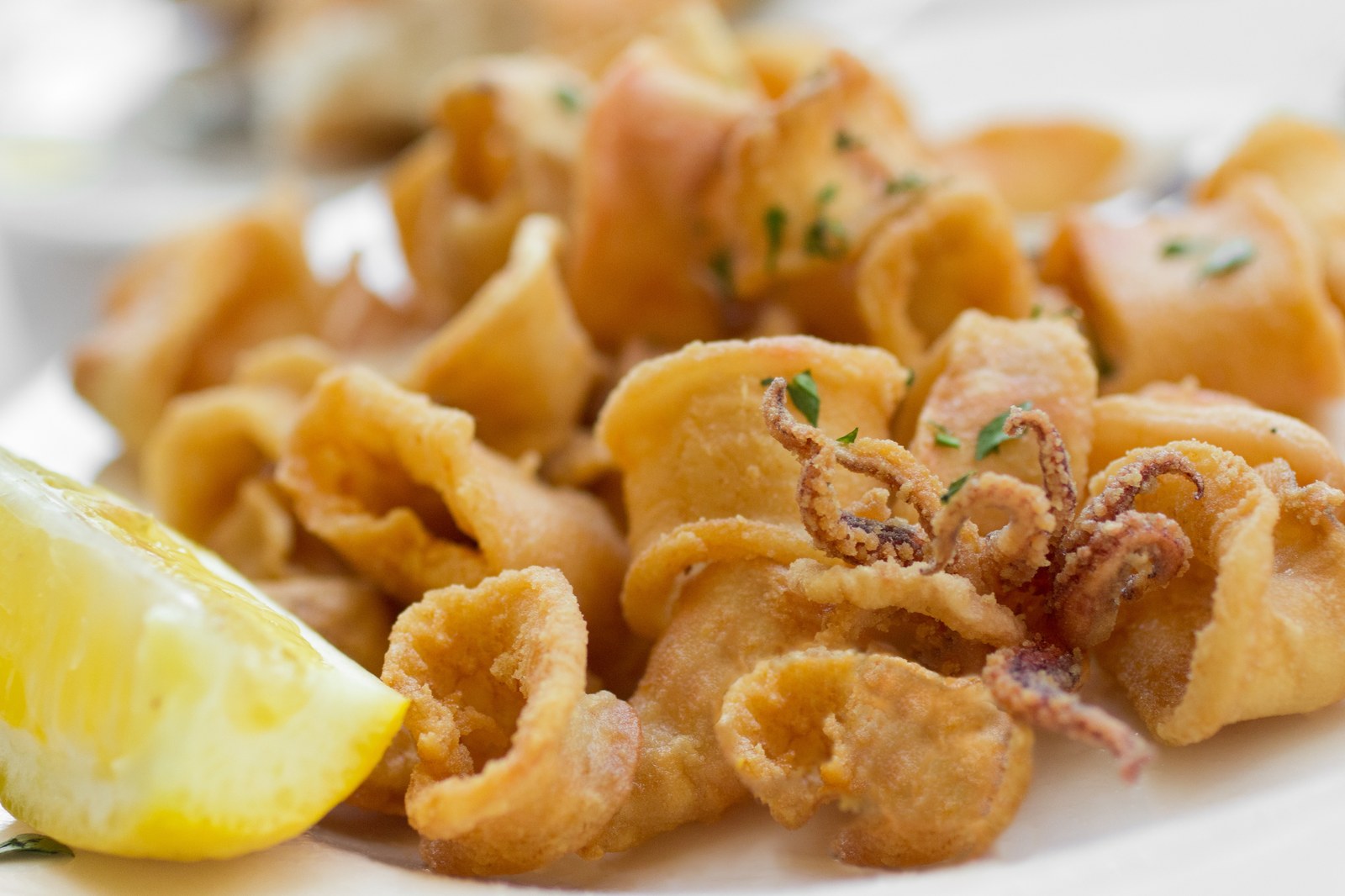 Plate of golden fried calamari rings and tentacles garnished with fresh parsley, served with a lemon wedge