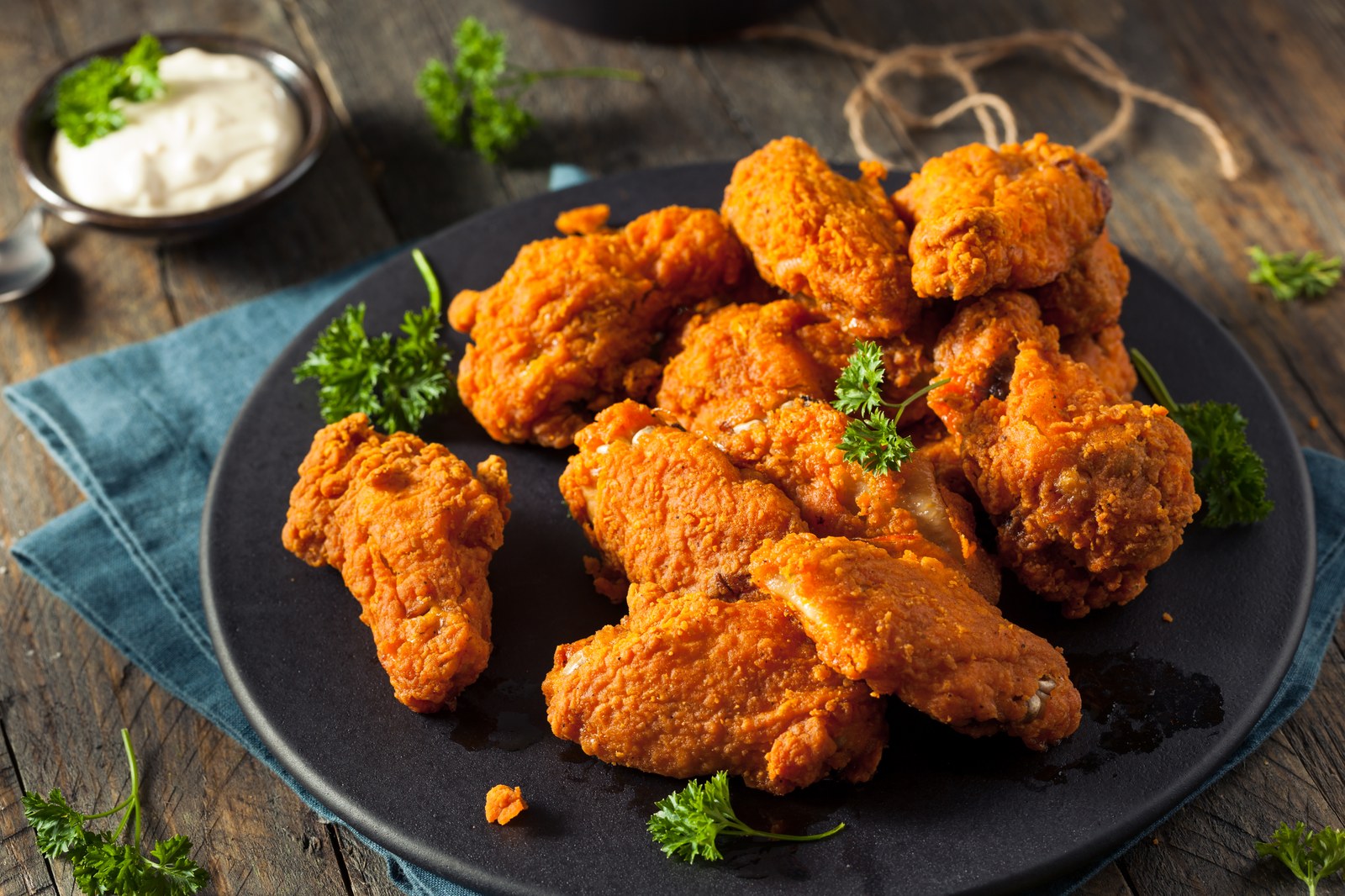 Golden brown fried chicken pieces with crispy textured coating piled on black plate with fresh parsley garnish and white dipping sauce in background