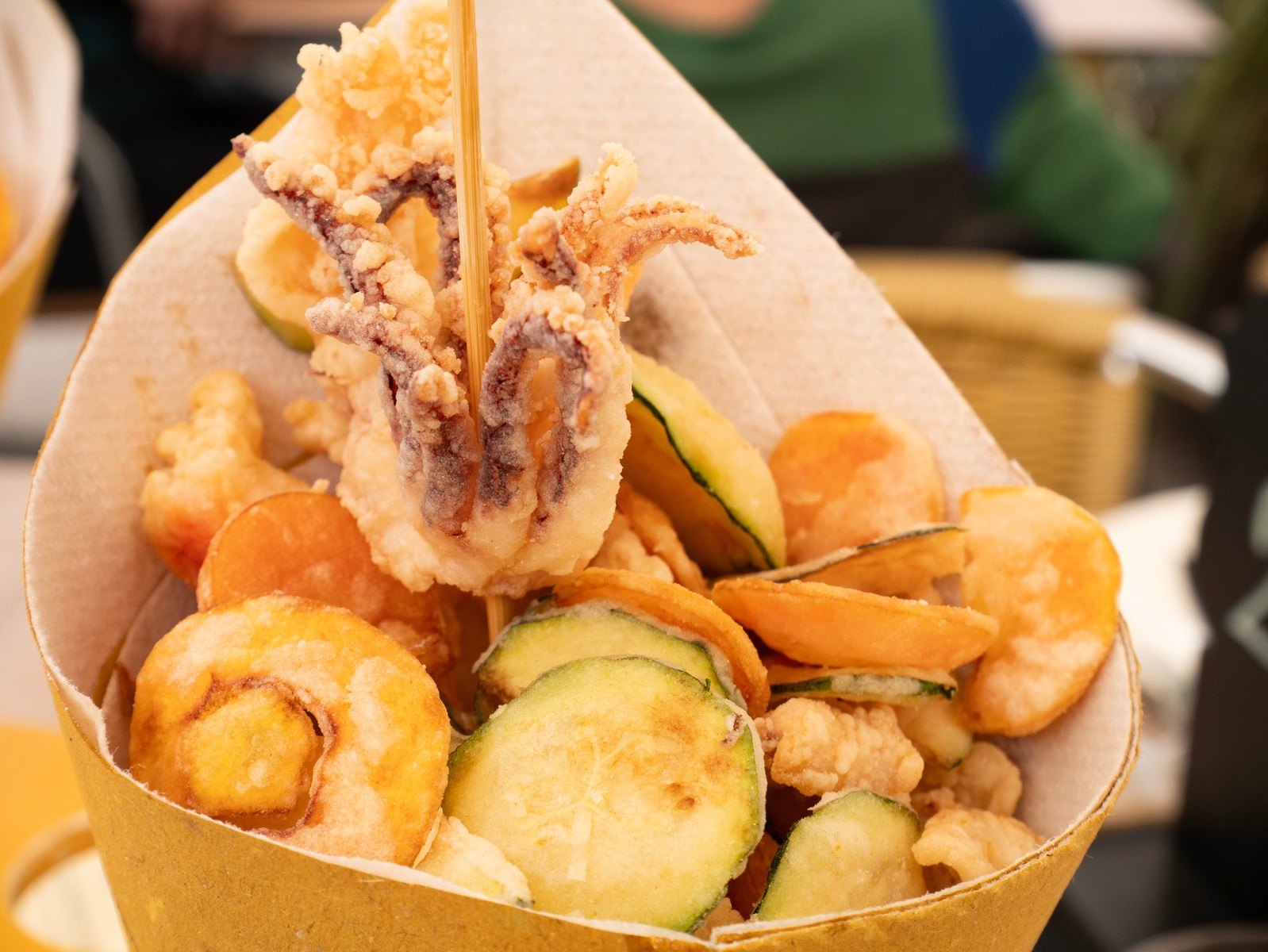 Italian fritto misto with battered and fried squid, shrimp, and zucchini slices in a paper cone