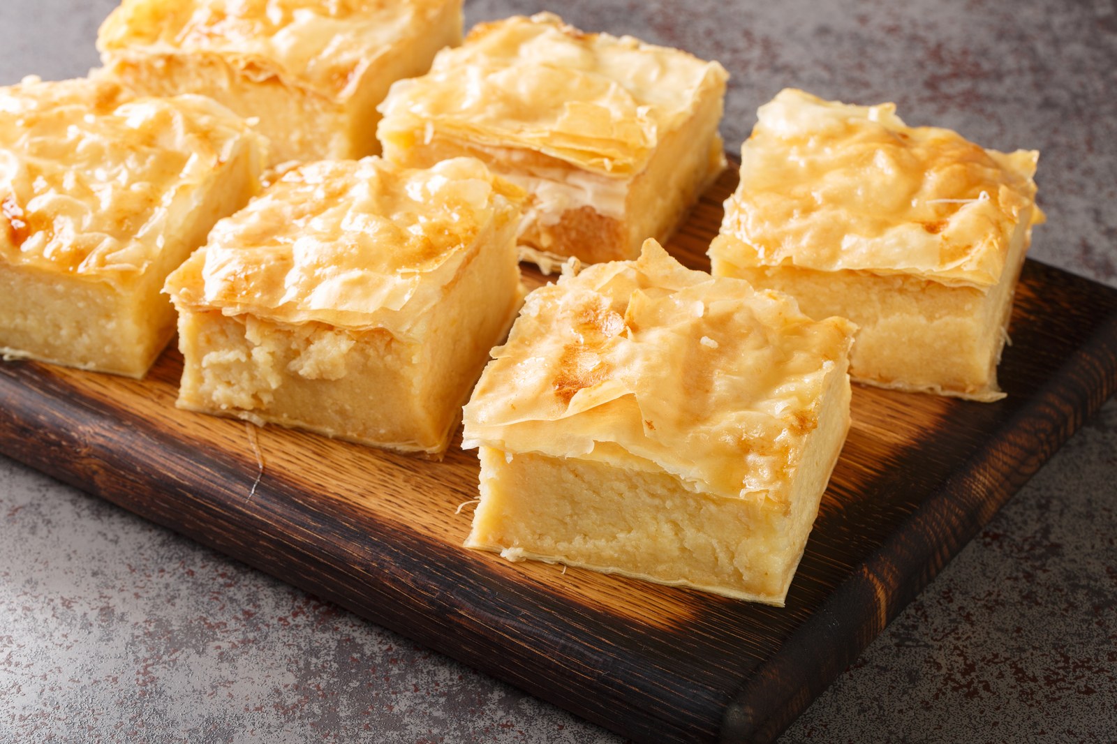 Greek galaktoboureko dessert cut into squares, showing layers of phyllo pastry with creamy custard filling and honey syrup glaze