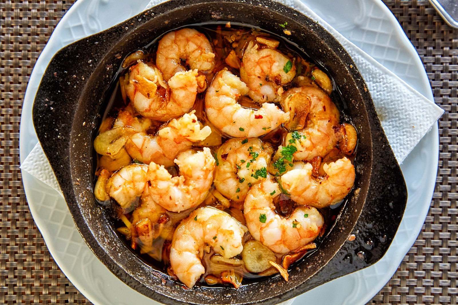 Pan of garlic butter shrimp with whole garlic cloves in a black skillet, garnished with fresh parsley