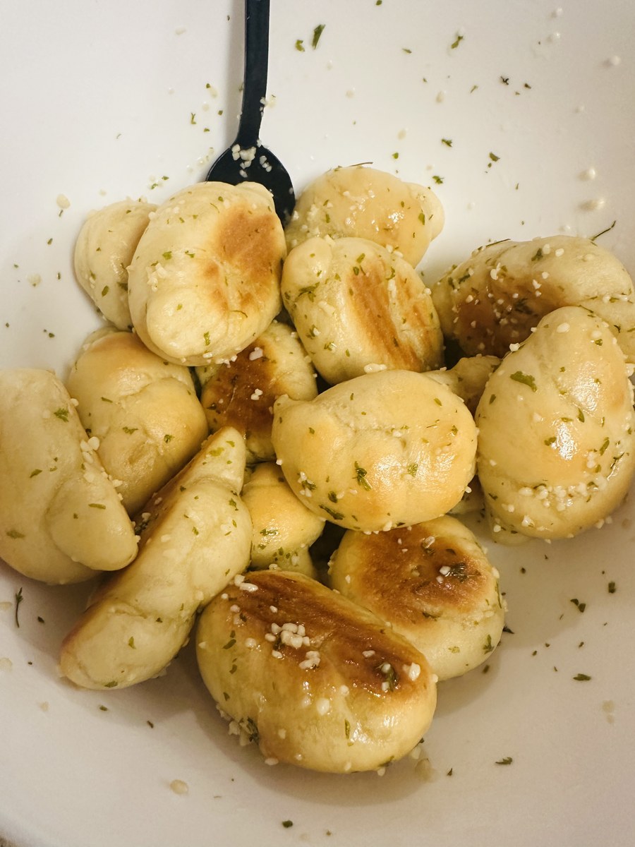 Pile of golden garlic knots brushed with butter, garlic, and herbs, sprinkled with parmesan cheese and sea salt
