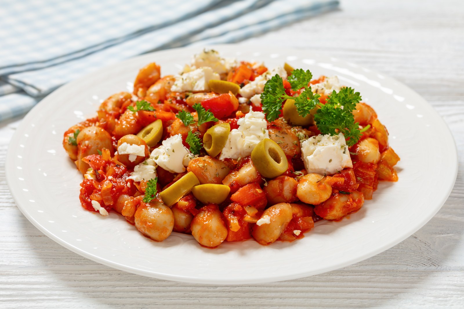 Greek gigantes plaki with large white beans in tomato sauce topped with feta cheese, olives, and fresh parsley
