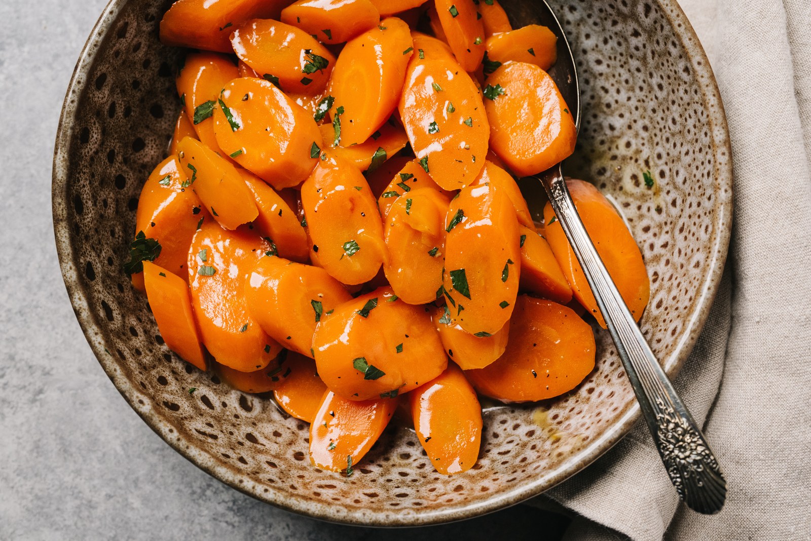 Bowl of glazed carrots cut on the diagonal, coated in a shiny butter glaze and garnished with fresh parsley