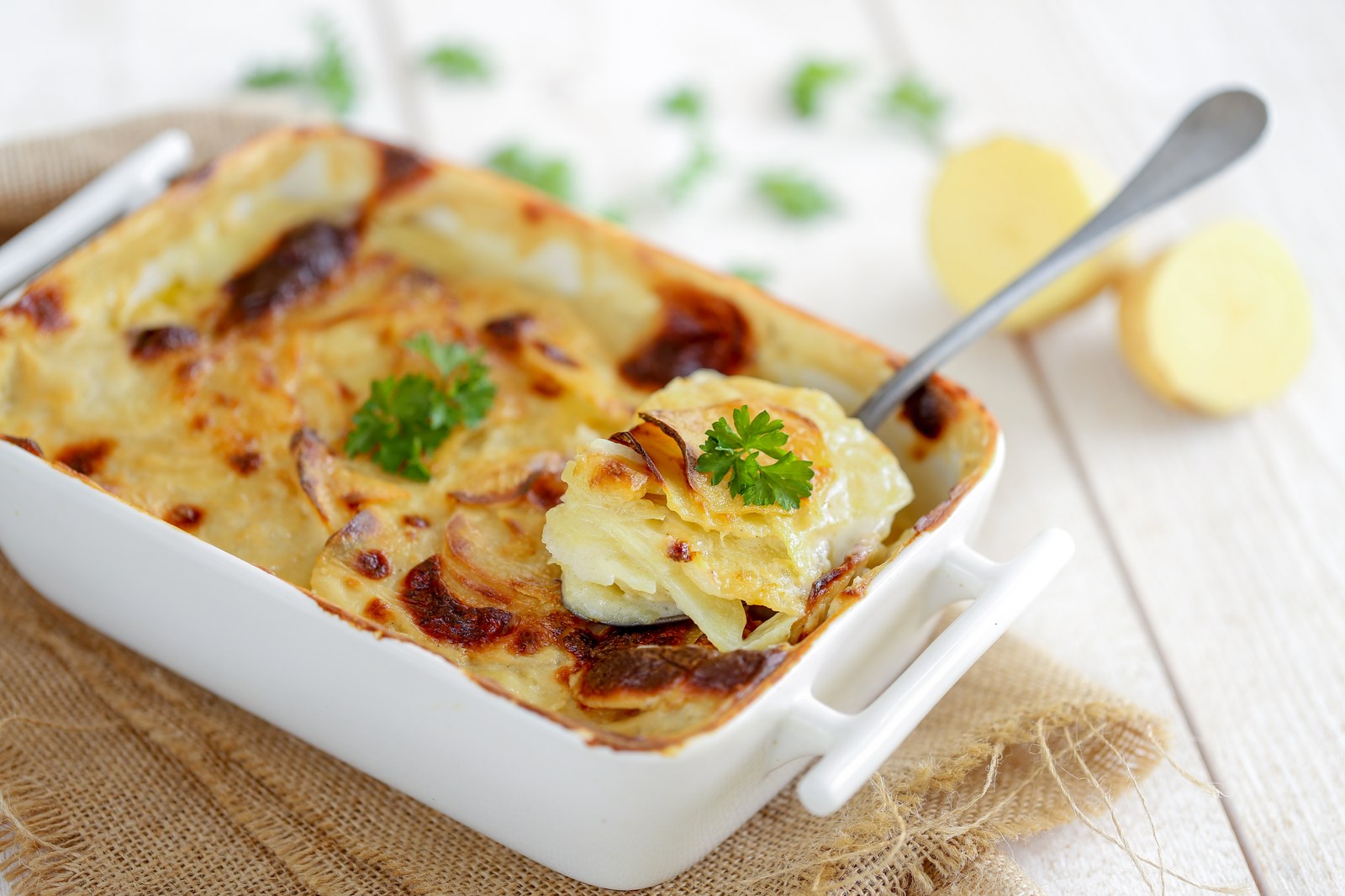 French potato gratin in a white baking dish showing layers of thinly sliced potatoes with golden bubbly cheese top