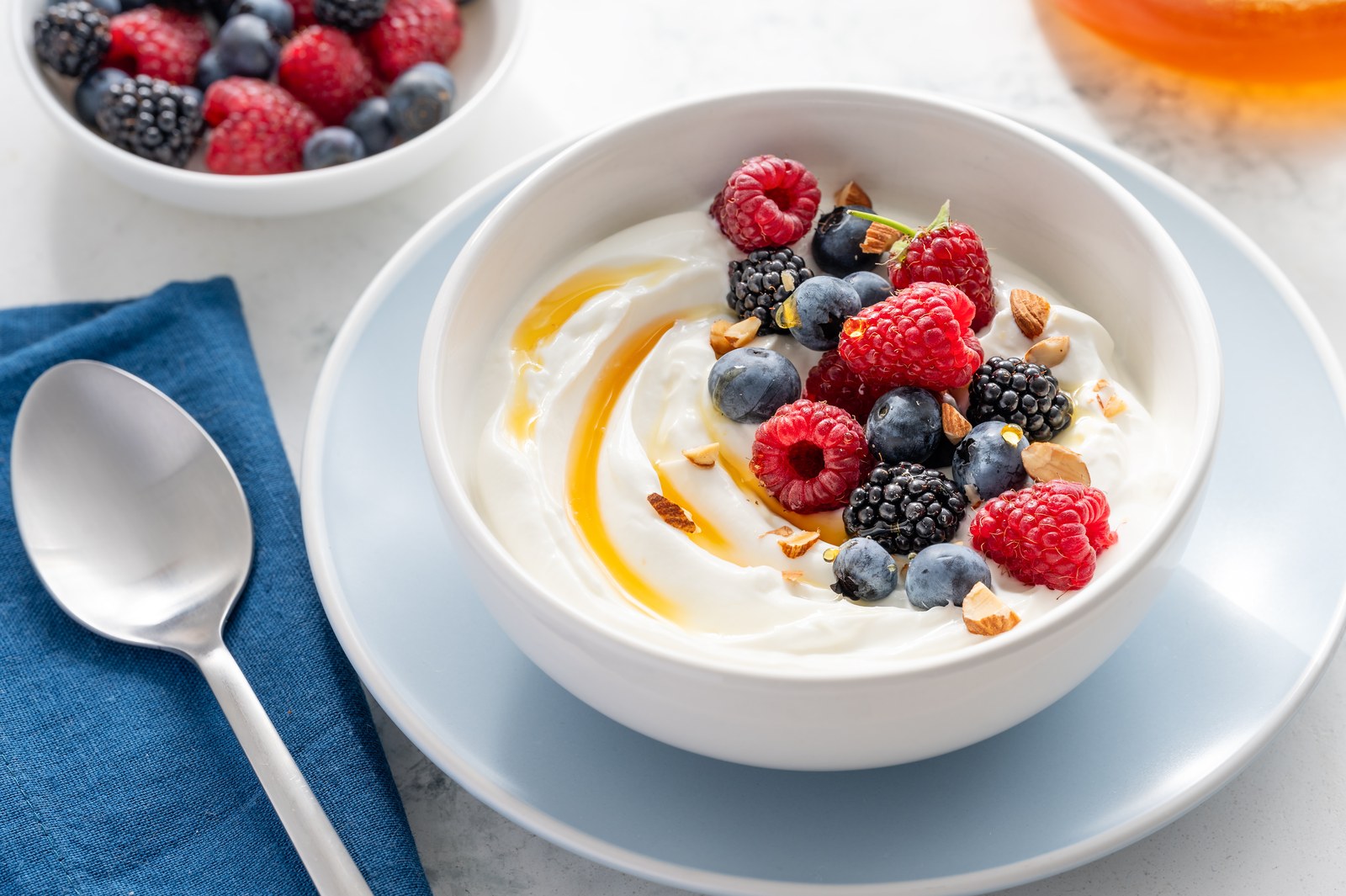 Bowl of thick Greek yogurt topped with fresh raspberries, blueberries, blackberries, sliced almonds, and a drizzle of honey