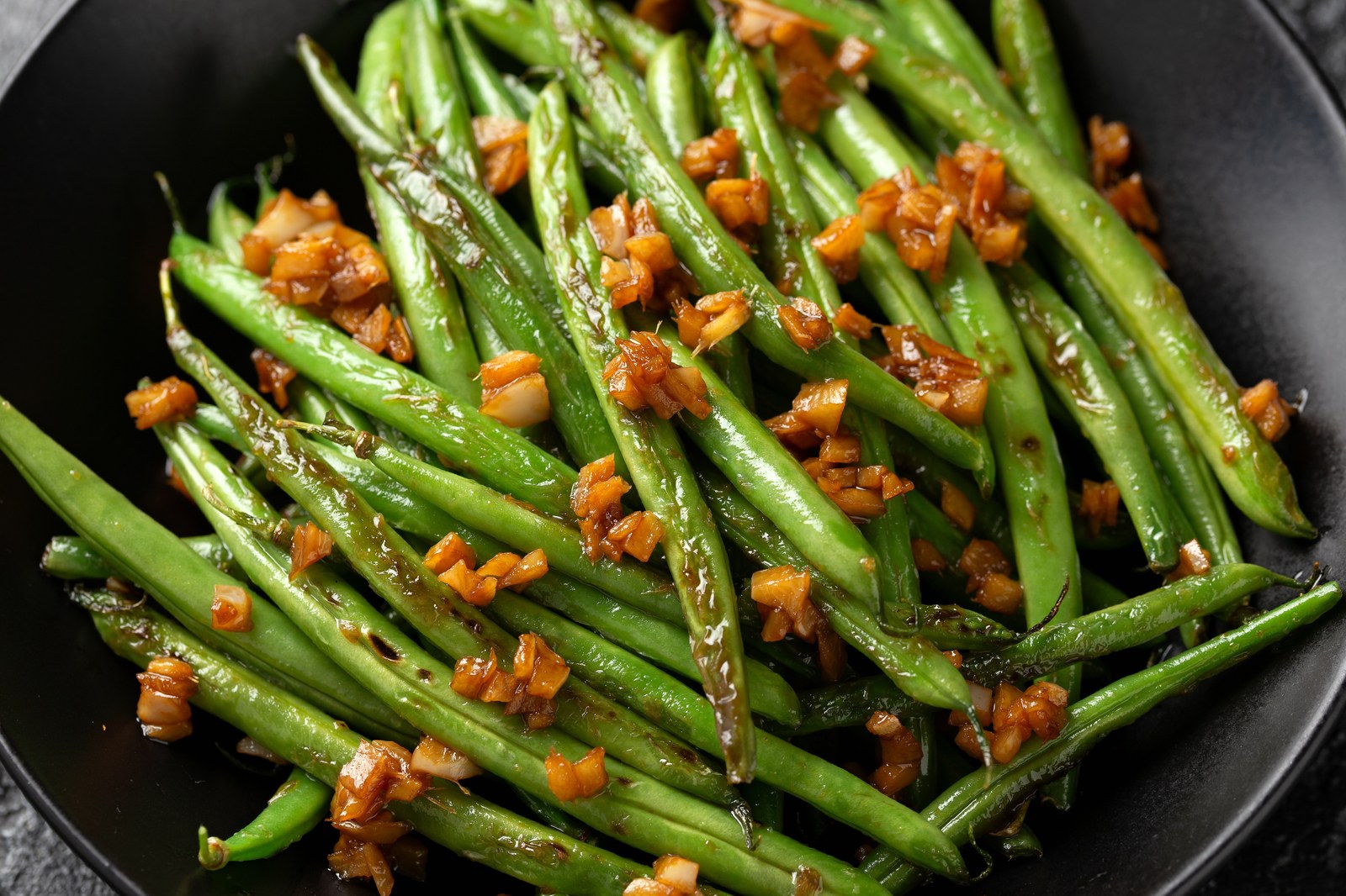 Sautéed green beans in a black pan with minced garlic, glistening with white wine butter sauce
