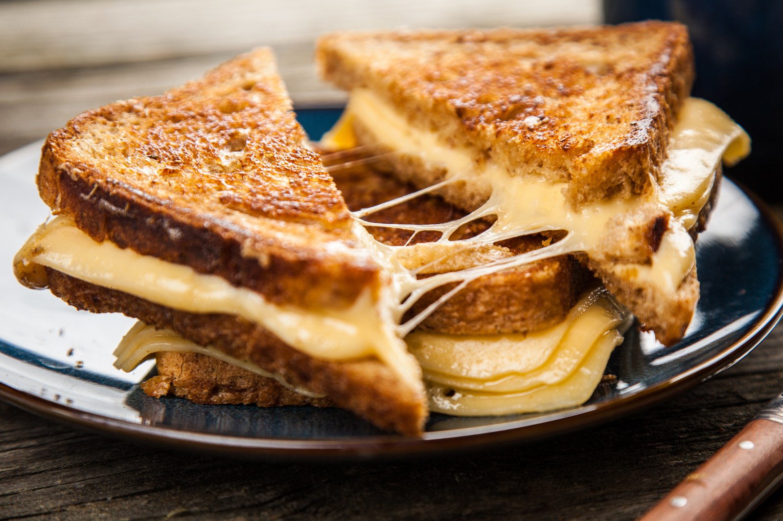 Golden-brown grilled cheese sandwich cut diagonally on blue plate with melted cheese stretching between halves