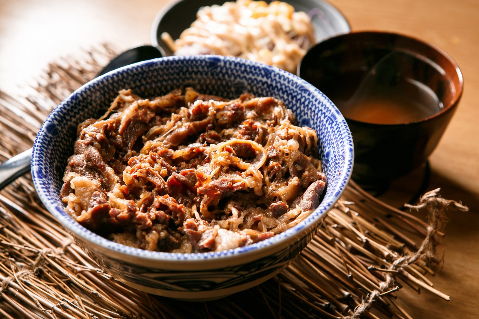 A bowl of thinly sliced beef and onions in savory sauce over white rice, presented in a decorative blue and white bowl