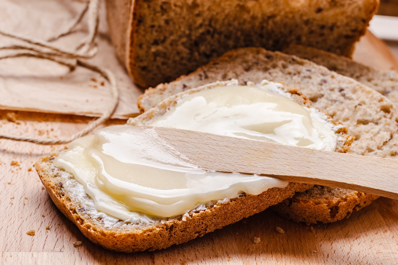 A slice of whole grain bread with creamy honey butter being spread with a wooden knife