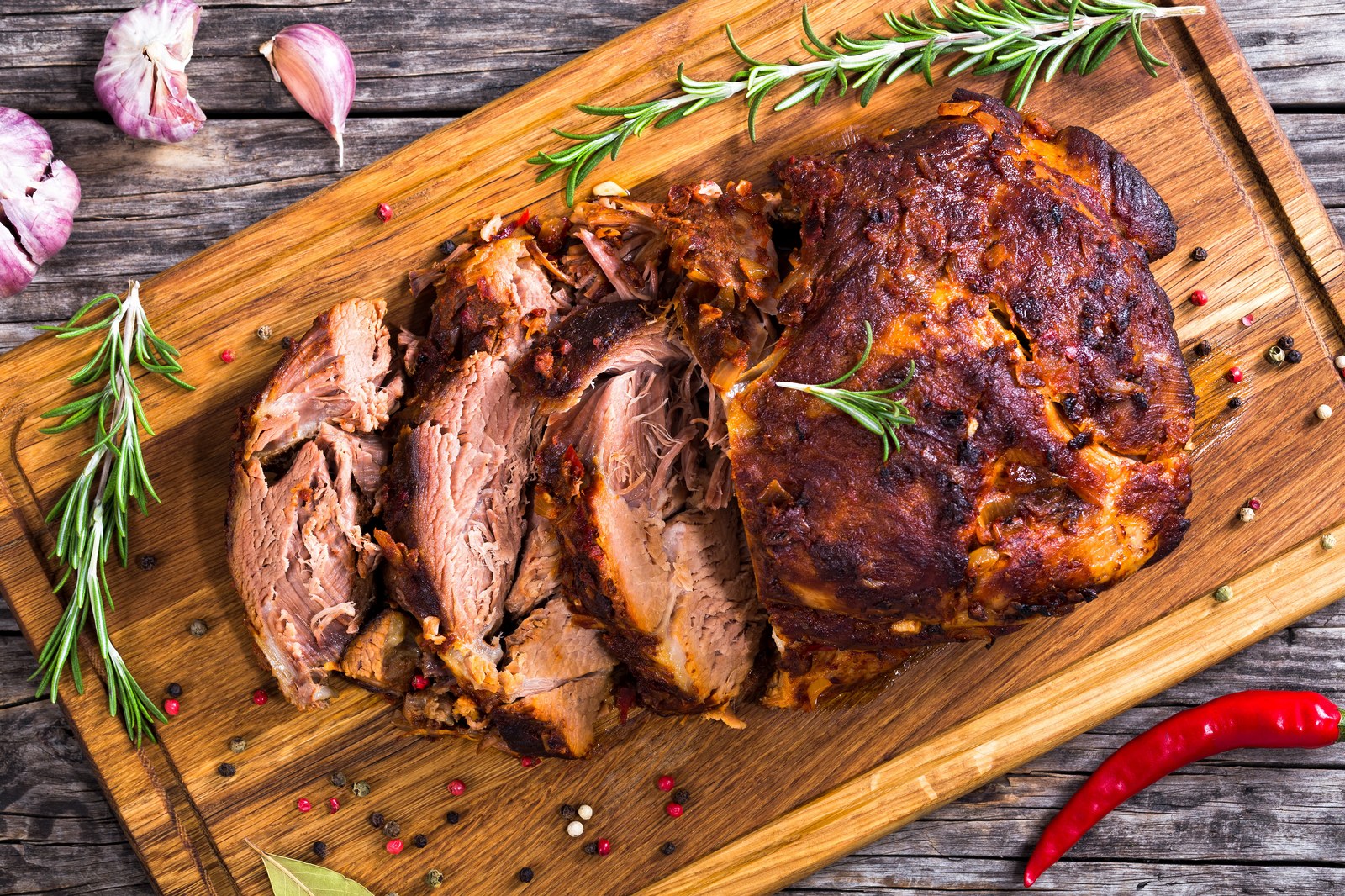 Sliced Italian pot roast on a wooden cutting board garnished with fresh rosemary and red chili pepper