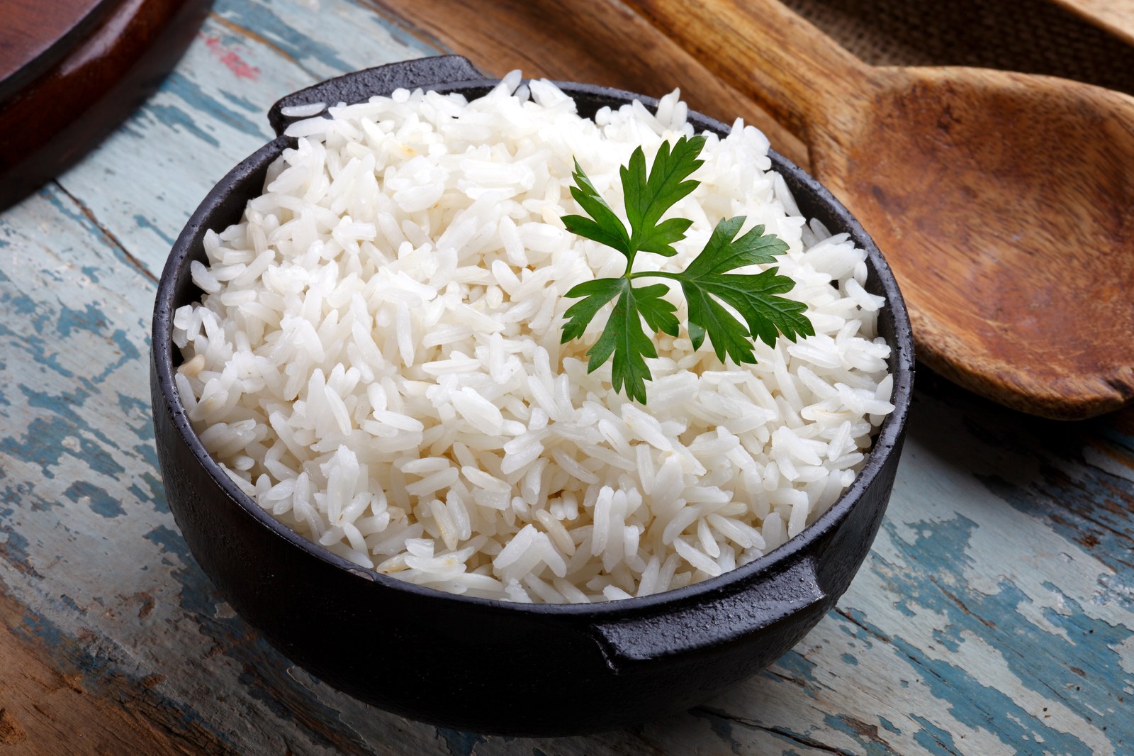 A rustic black bowl filled with fluffy white jasmine rice garnished with a sprig of fresh parsley