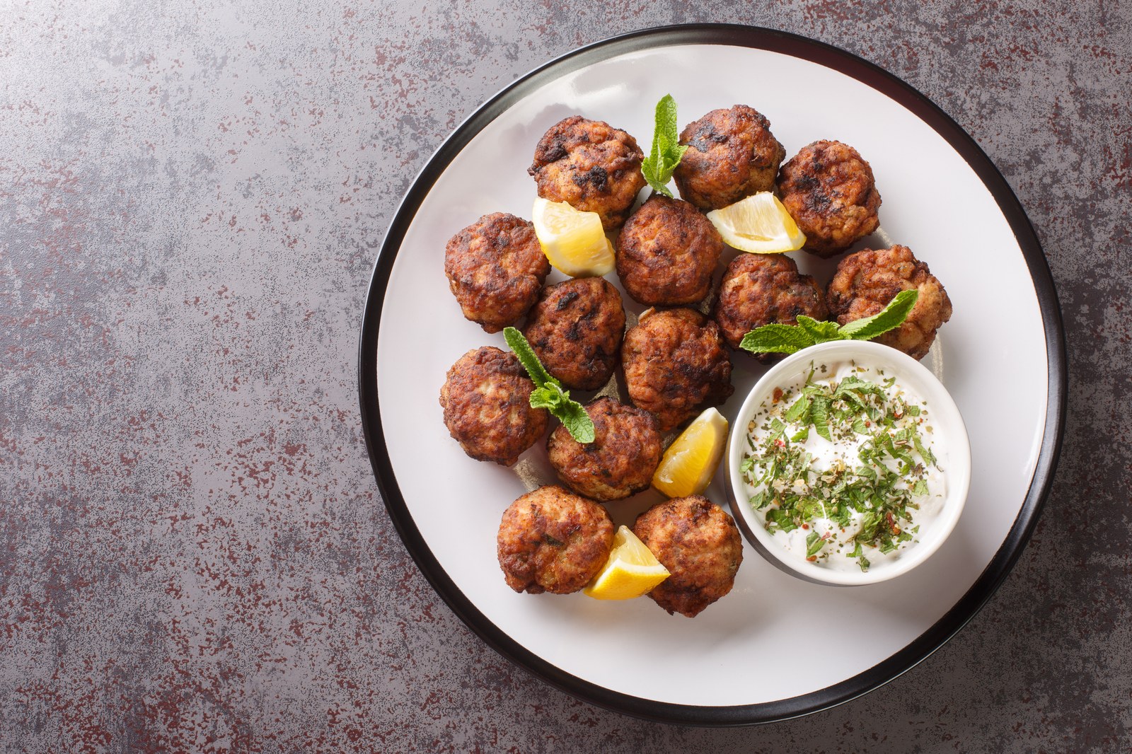 A plate of Greek meatballs garnished with fresh parsley served with pita bread, olives, olive oil, and fresh vegetables