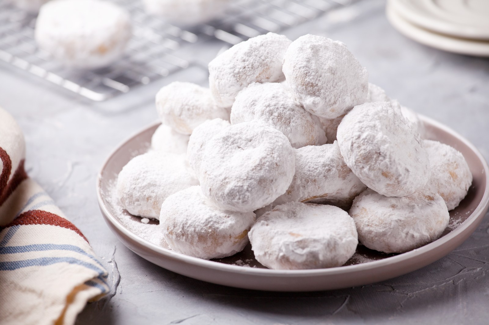 A plate stacked high with round Greek butter cookies heavily dusted with powdered sugar
