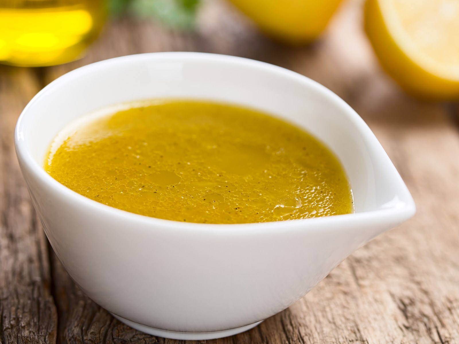 A white pour dish filled with bright yellow lemon olive oil dressing with visible black pepper specks