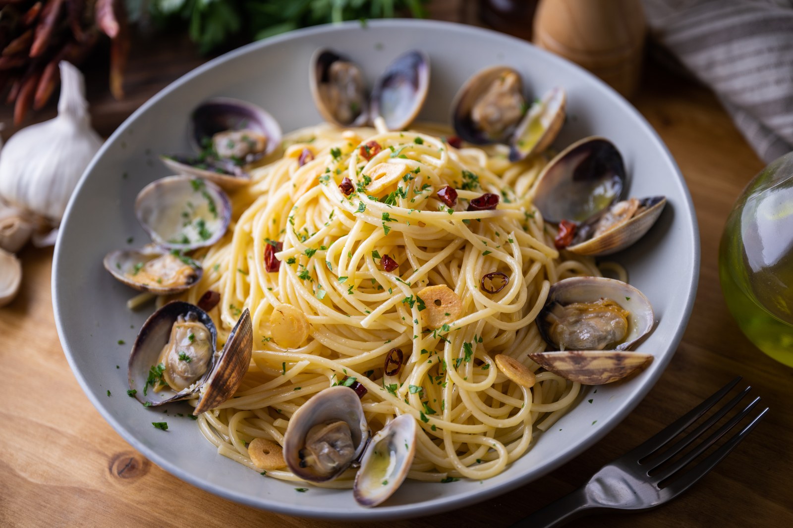 A white bowl of linguine pasta tossed with fresh clams in their shells, garlic, olive oil, parsley, and red pepper flakes