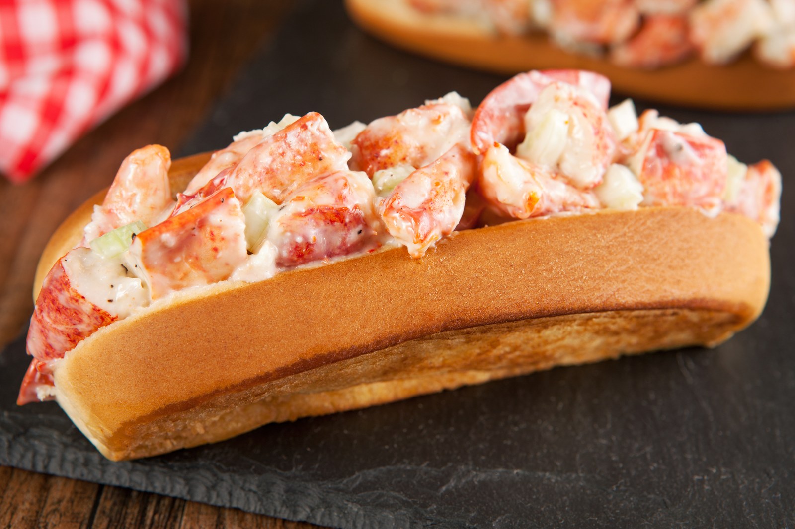 A fresh lobster roll filled with chunks of lobster meat dressed in mayonnaise on a toasted split top bun served on a dark slate board