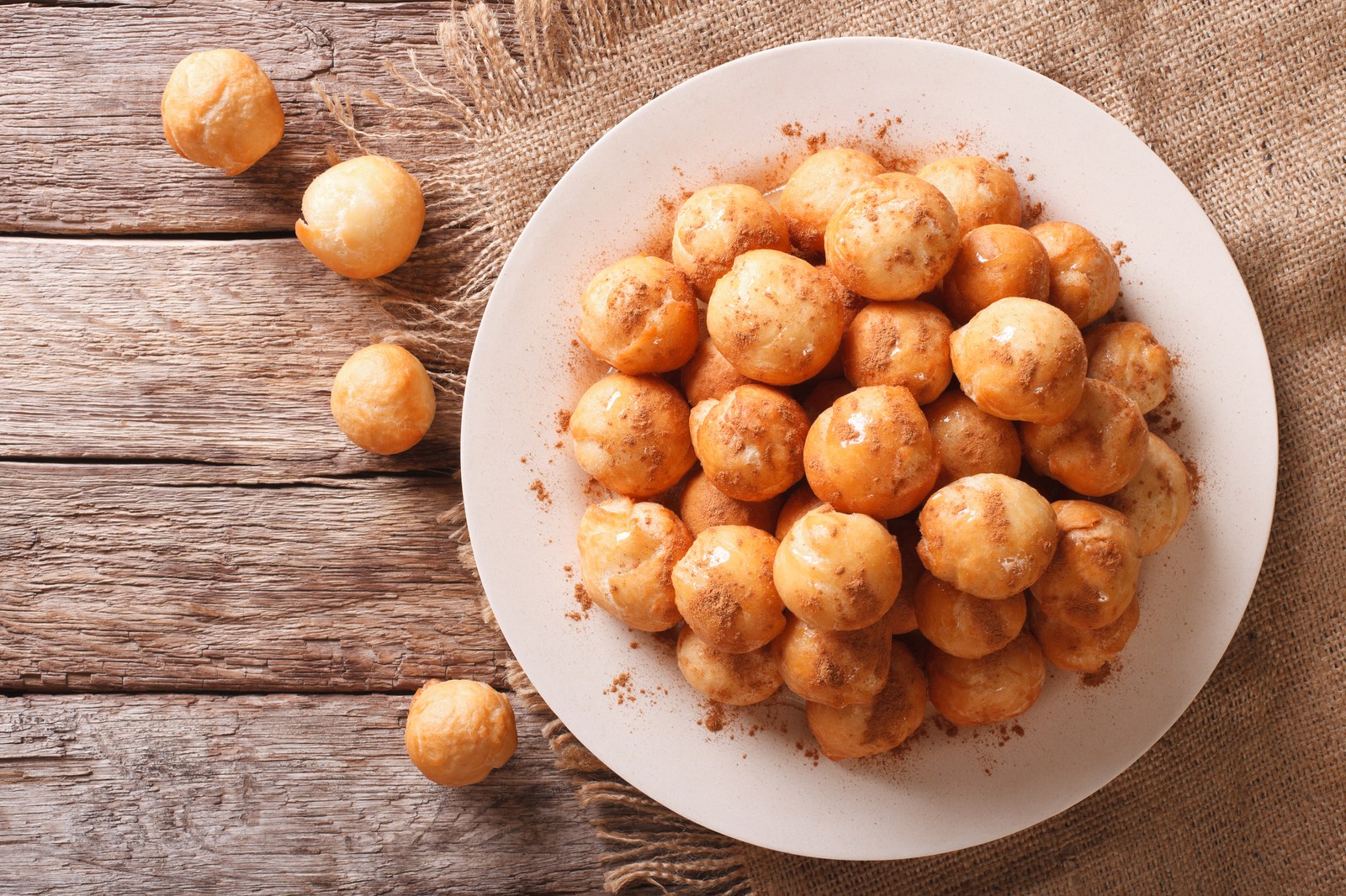 A white plate piled with golden fried Greek doughnut holes dusted with cinnamon powder