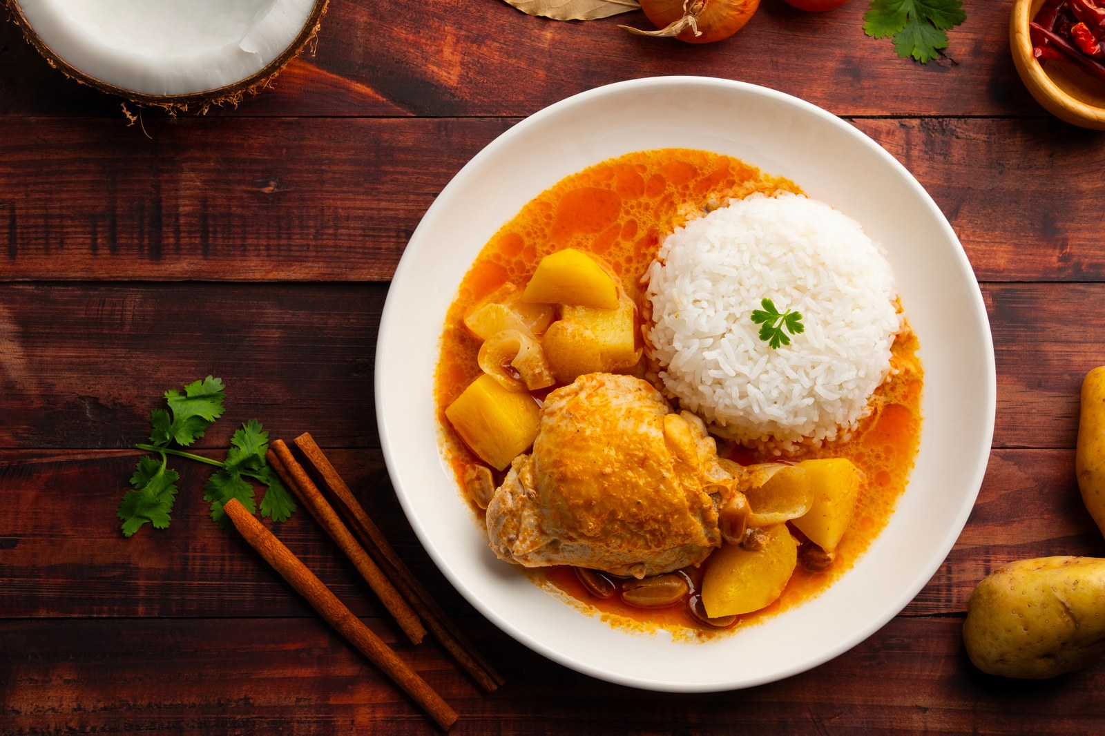 A white bowl of Thai massaman curry with chicken, potatoes, and cashews in rich coconut curry sauce served with white rice