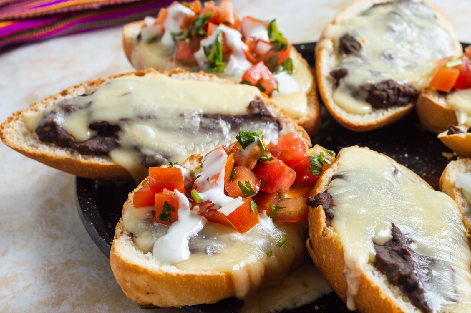 Open-faced bolillo rolls topped with refried beans, melted cheese, and pico de gallo