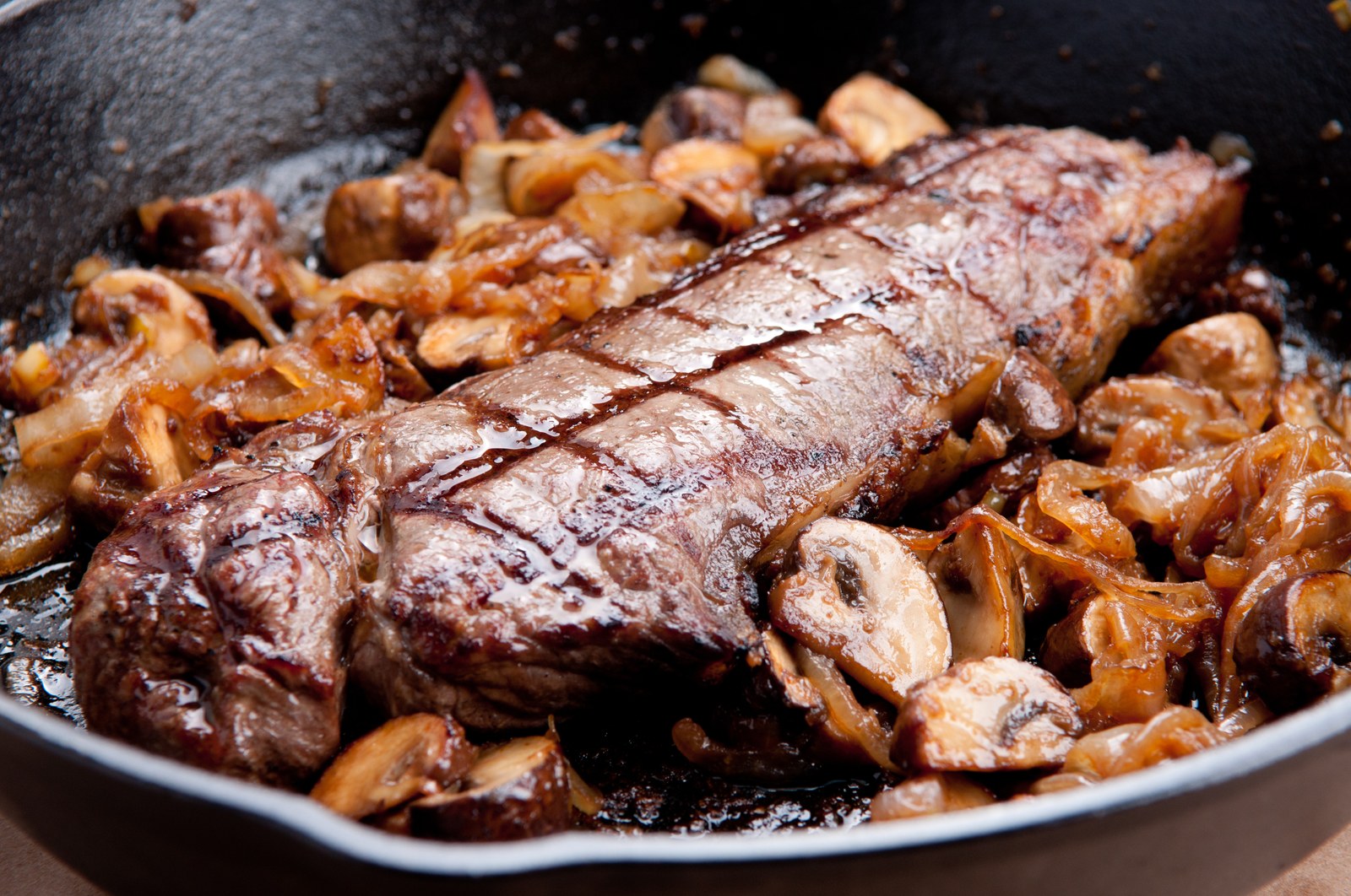 Seared strip steak resting on a bed of caramelized mushrooms and onions