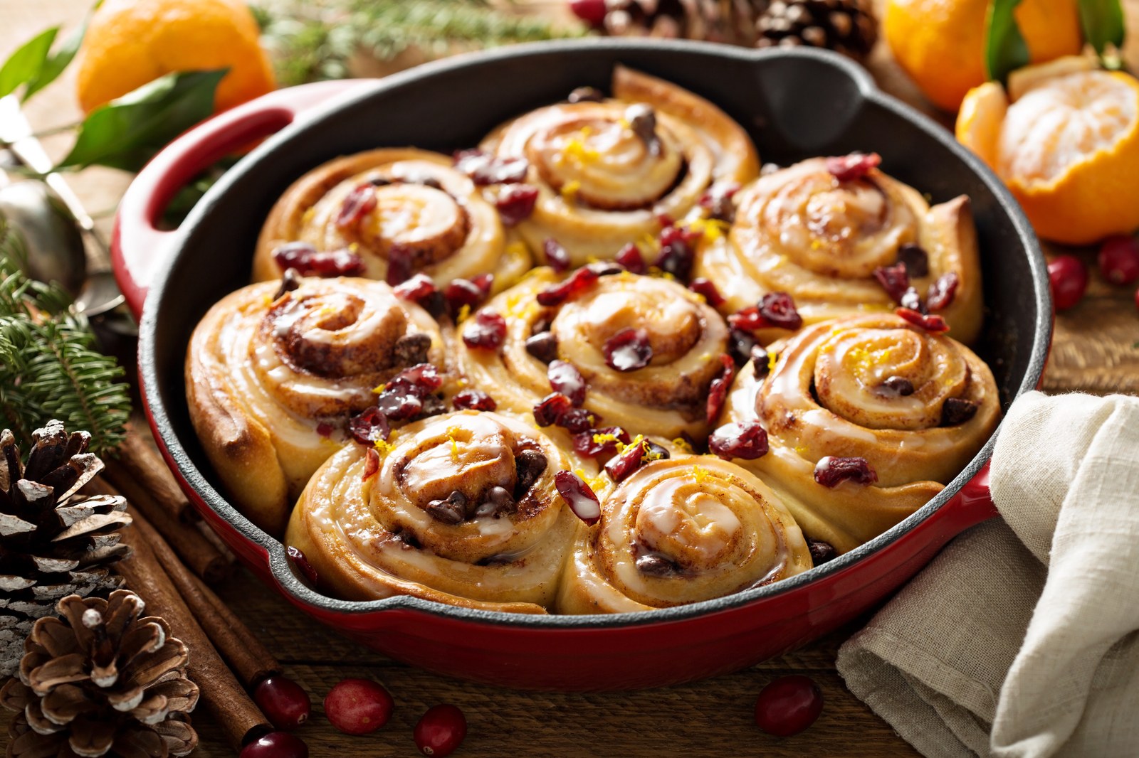 Cinnamon rolls in a cast iron skillet topped with cranberries, orange zest, and glaze