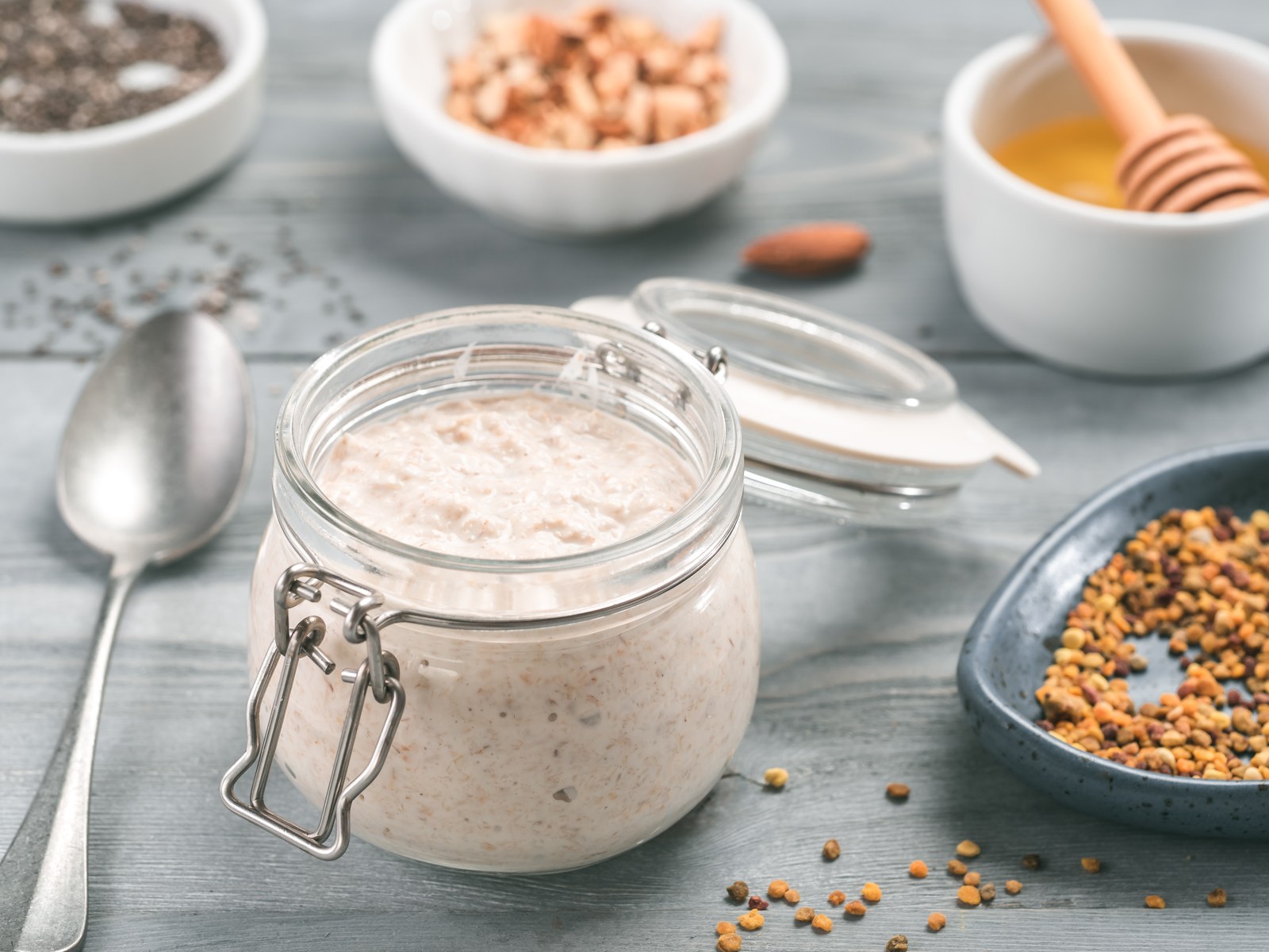 Overnight oats in glass jar with creamy texture, visible oat flakes, chia seeds, cinnamon swirl, honey and nuts in background on light blue surface