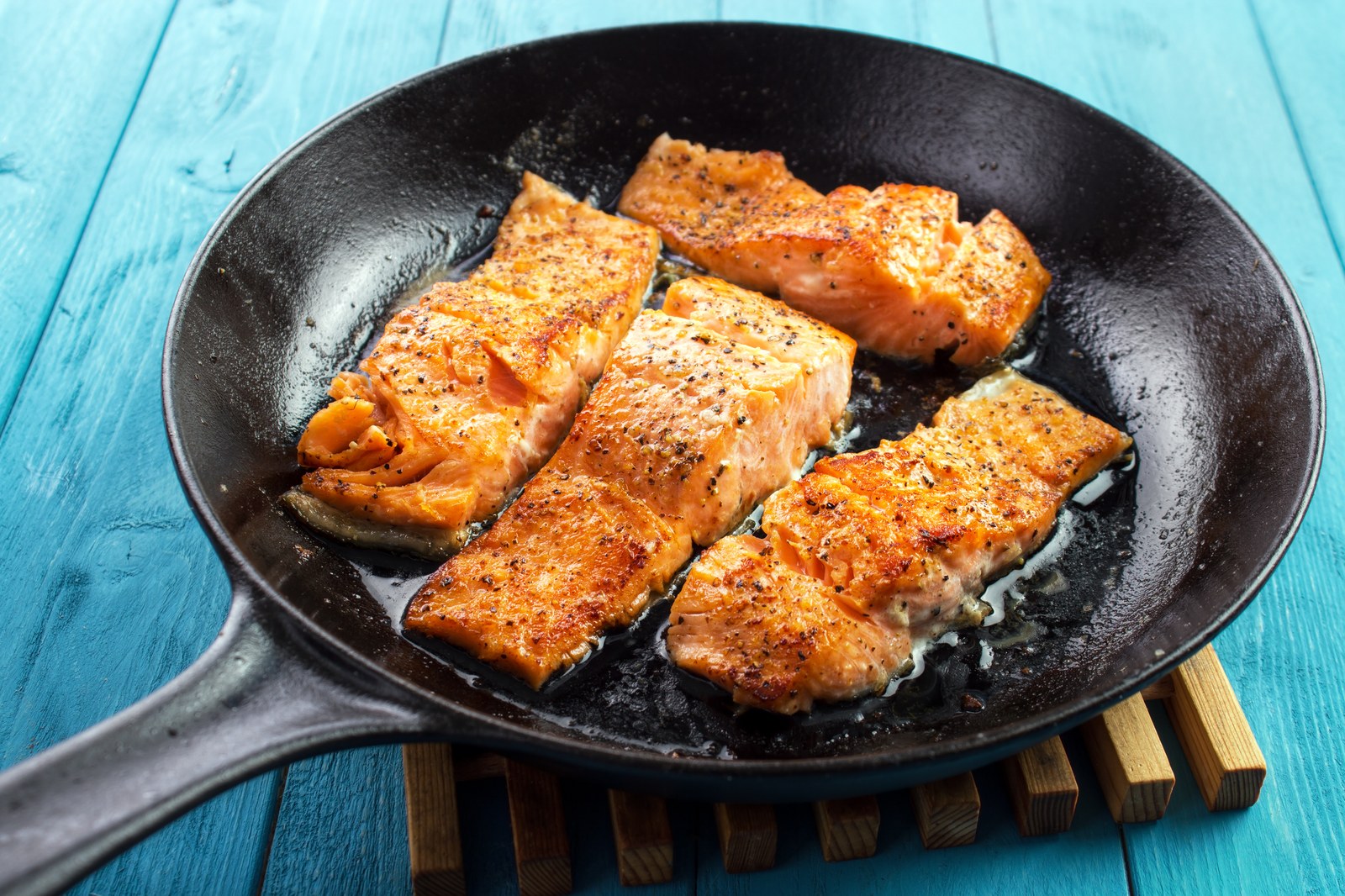 Four salmon fillets with golden crispy skin in a cast iron skillet