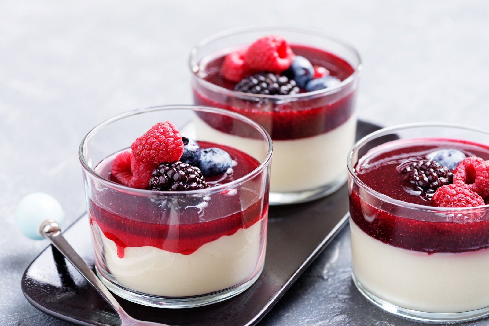 Three glasses of vanilla panna cotta topped with berry compote and fresh berries