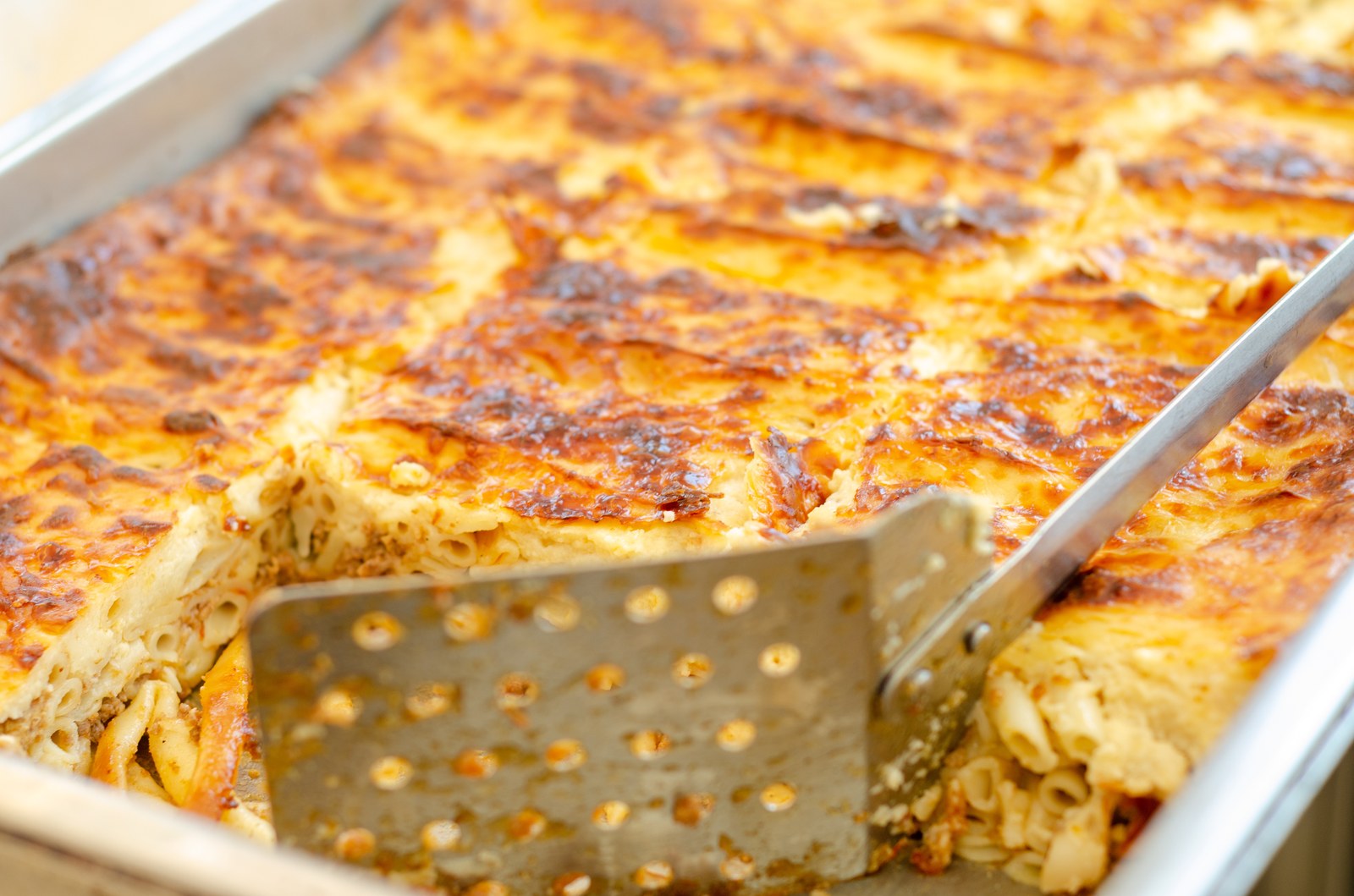 Greek pastitsio casserole with golden béchamel topping being served with a metal spatula