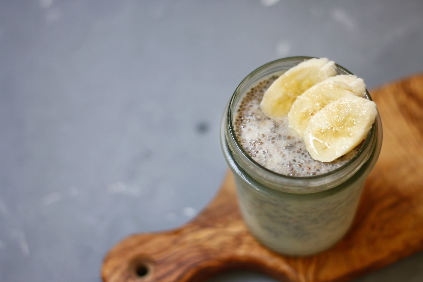 Mason jar filled with overnight oats topped with banana slices on a wooden cutting board