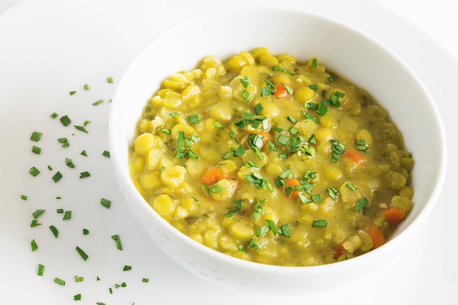 White bowl filled with green peas in a creamy yellow sauce, garnished with fresh chives