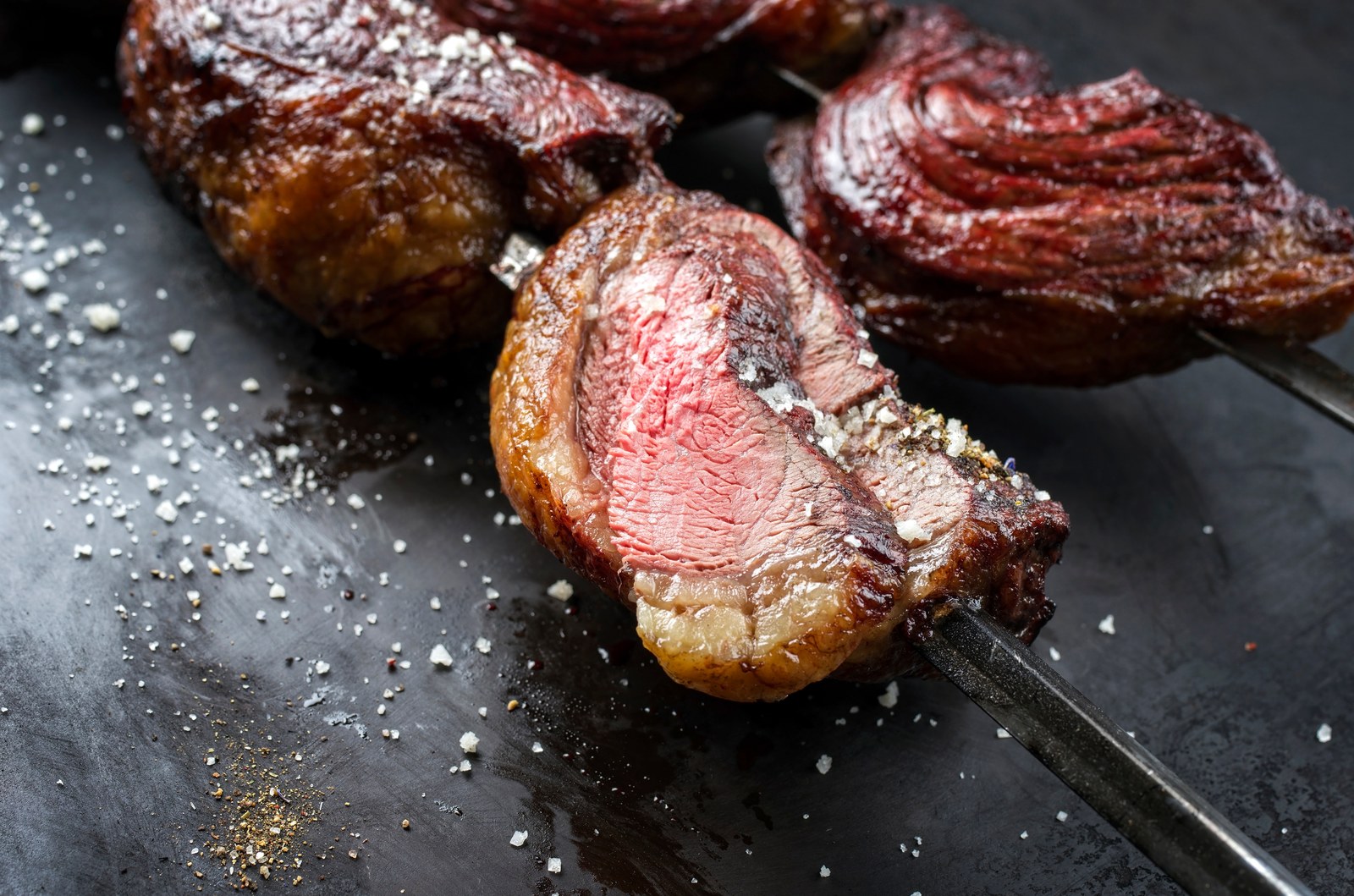 Sliced Brazilian picanha steak on a slate showing medium rare interior with coarse salt crystals