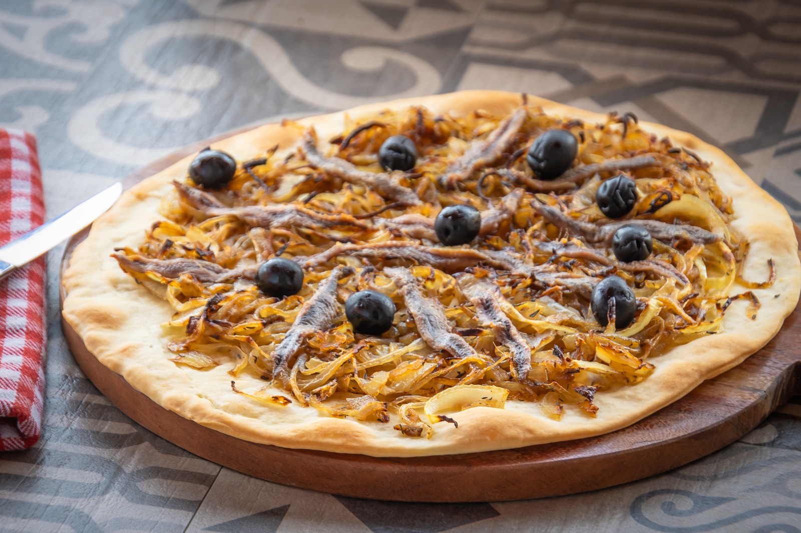 French onion tart topped with caramelized onions, anchovies, and black olives on a wooden board