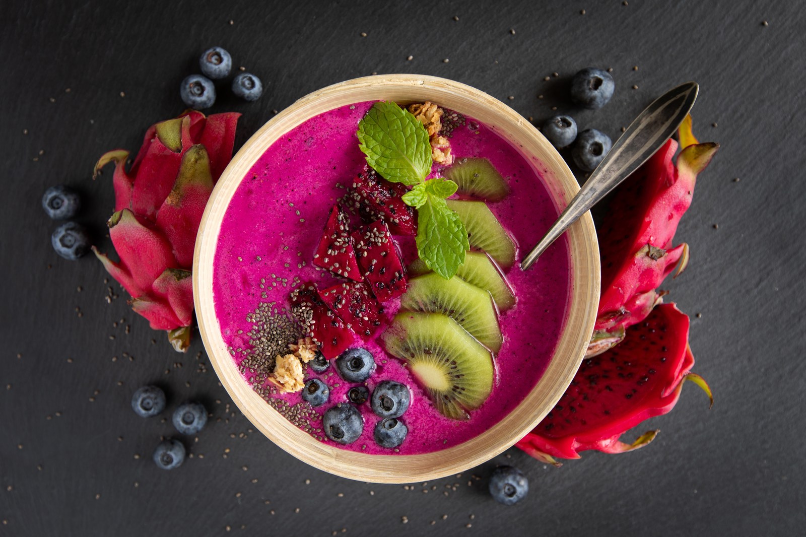 Bright pitaya bowl topped with fresh fruit, seeds, and a mint garnish