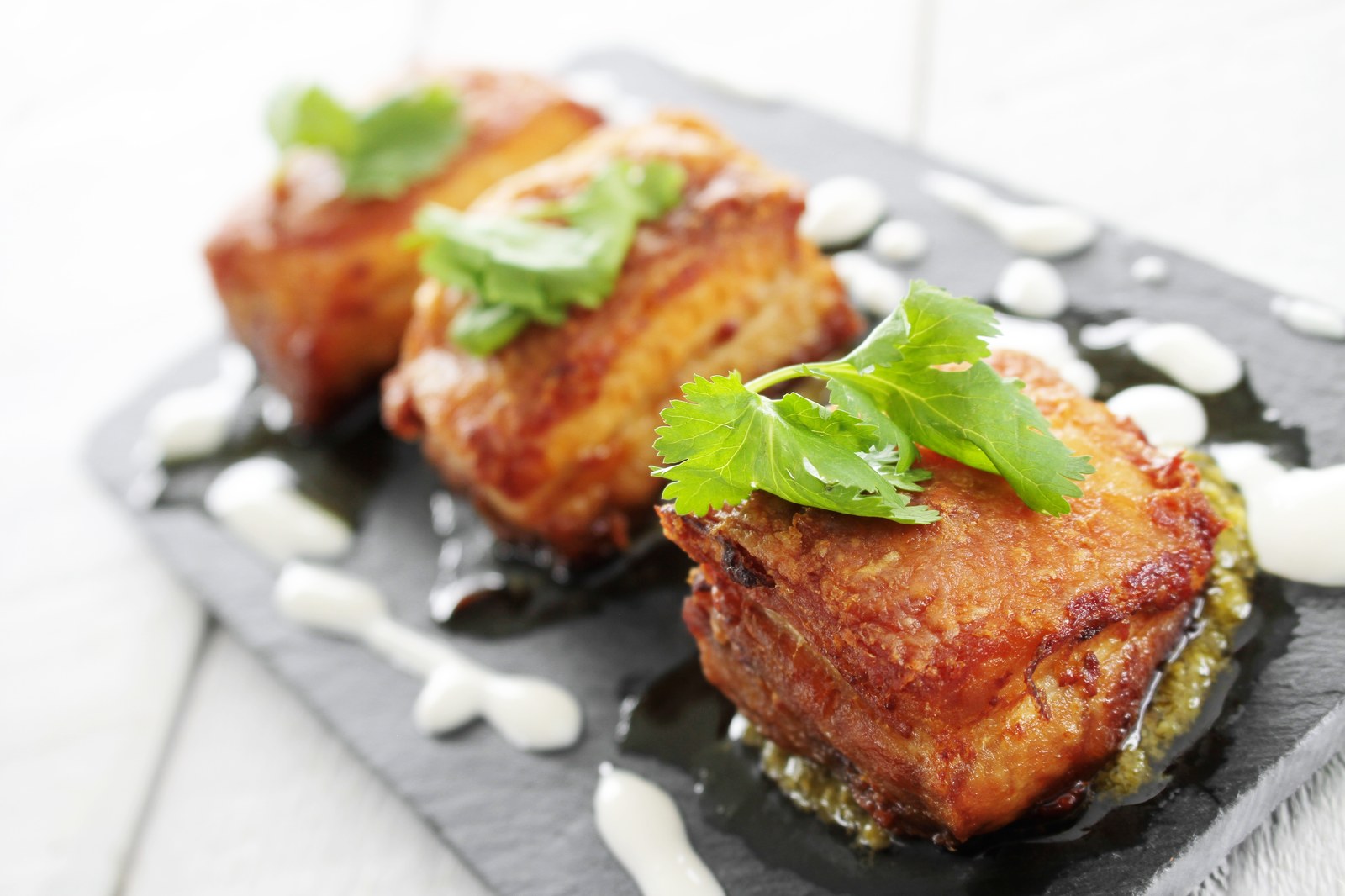 Crispy cubes of pork belly on a slate plate garnished with fresh cilantro and drizzled sauce