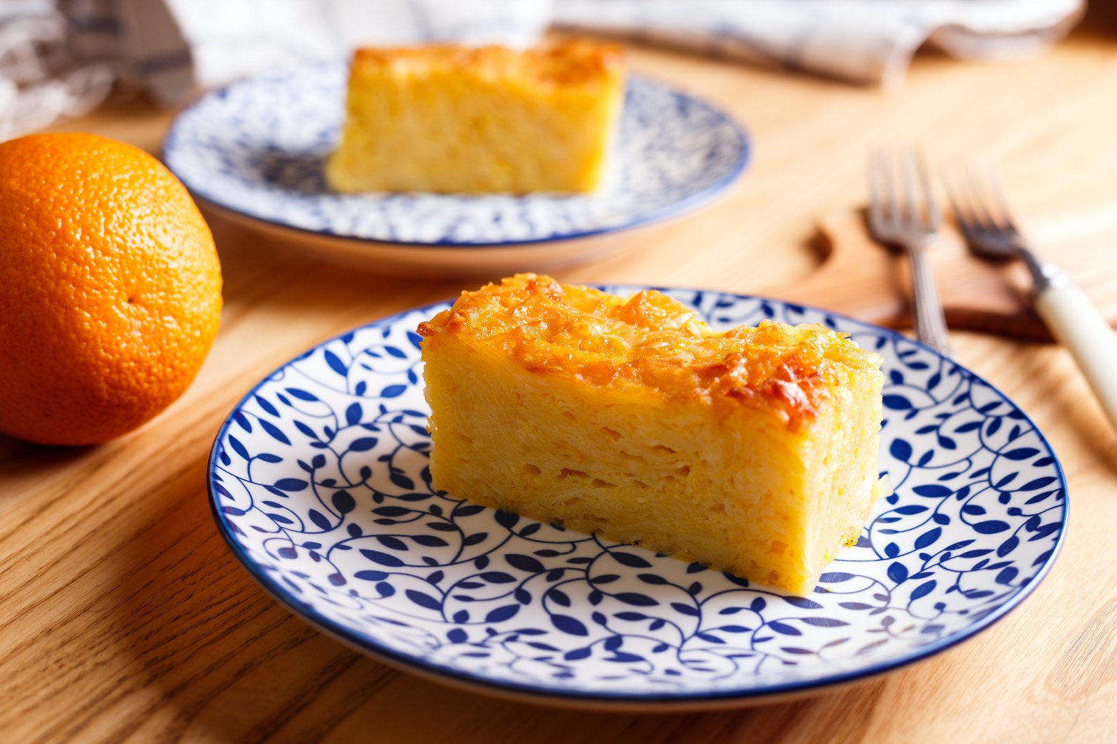 Slice of Greek orange phyllo cake on a blue and white plate with a whole orange beside it